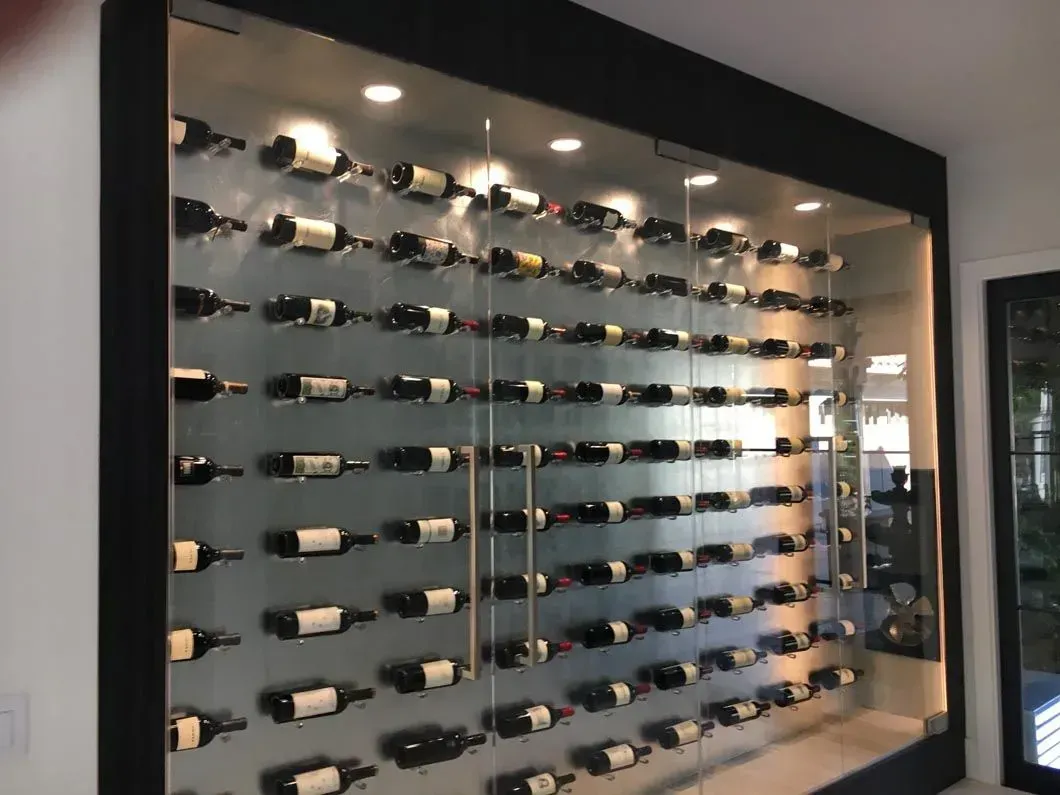Wine bottles displayed on a modern, wall-mounted rack behind glass, with overhead lighting.