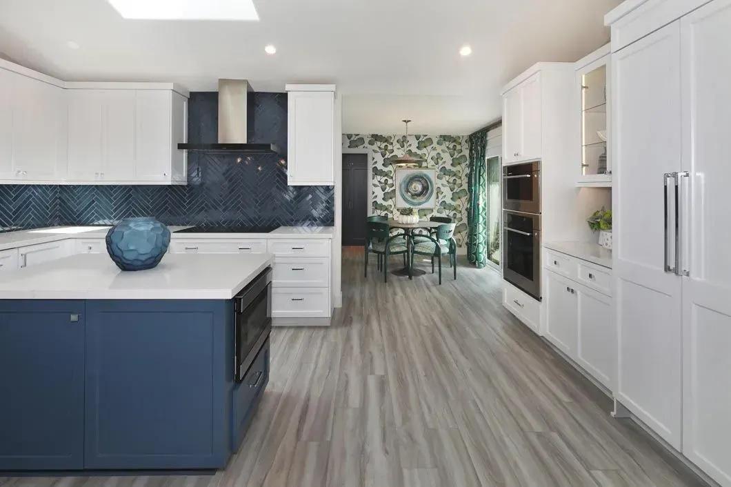 Modern kitchen with white and blue cabinets, island, and dining area with green patterned wallpaper.
