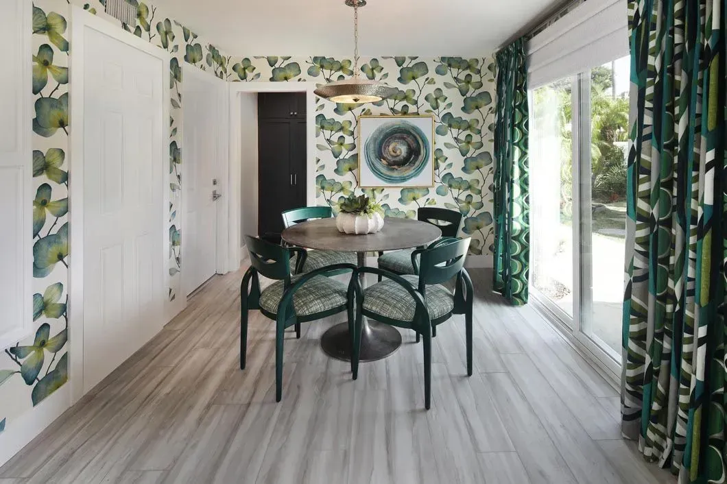 Dining room with floral wallpaper, round table, green chairs, and marble-look floor.
