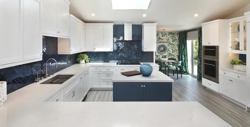 White and blue modern kitchen with an island, dark blue backsplash, and a view into a dining area.