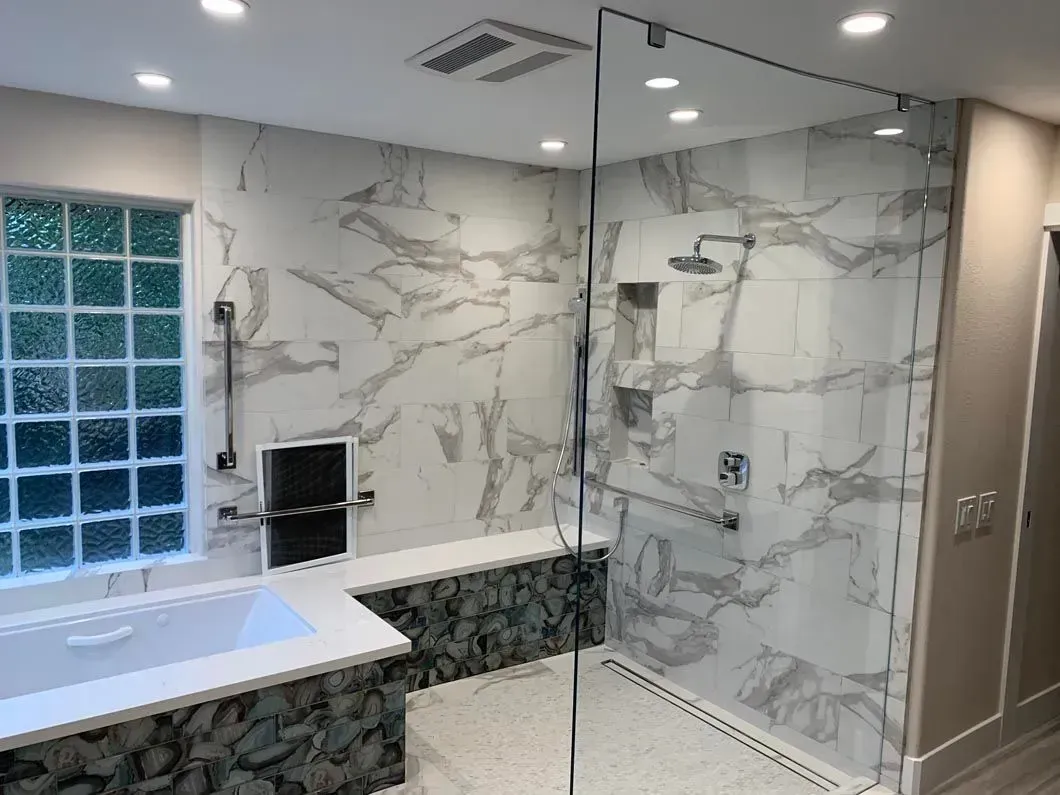 Modern bathroom with marble-look tiled walls, glass shower, built-in tub, and window.
