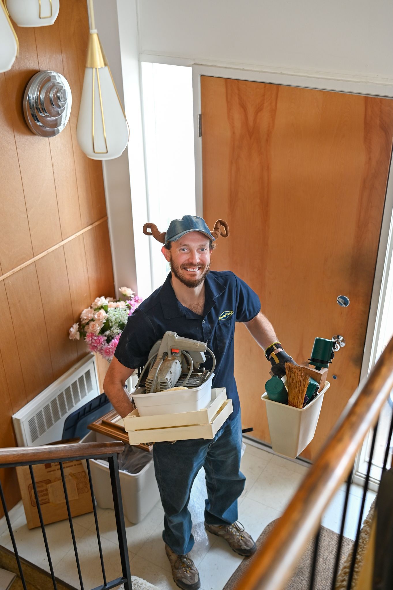 A man is standing on a staircase holding a crate and a bucket.