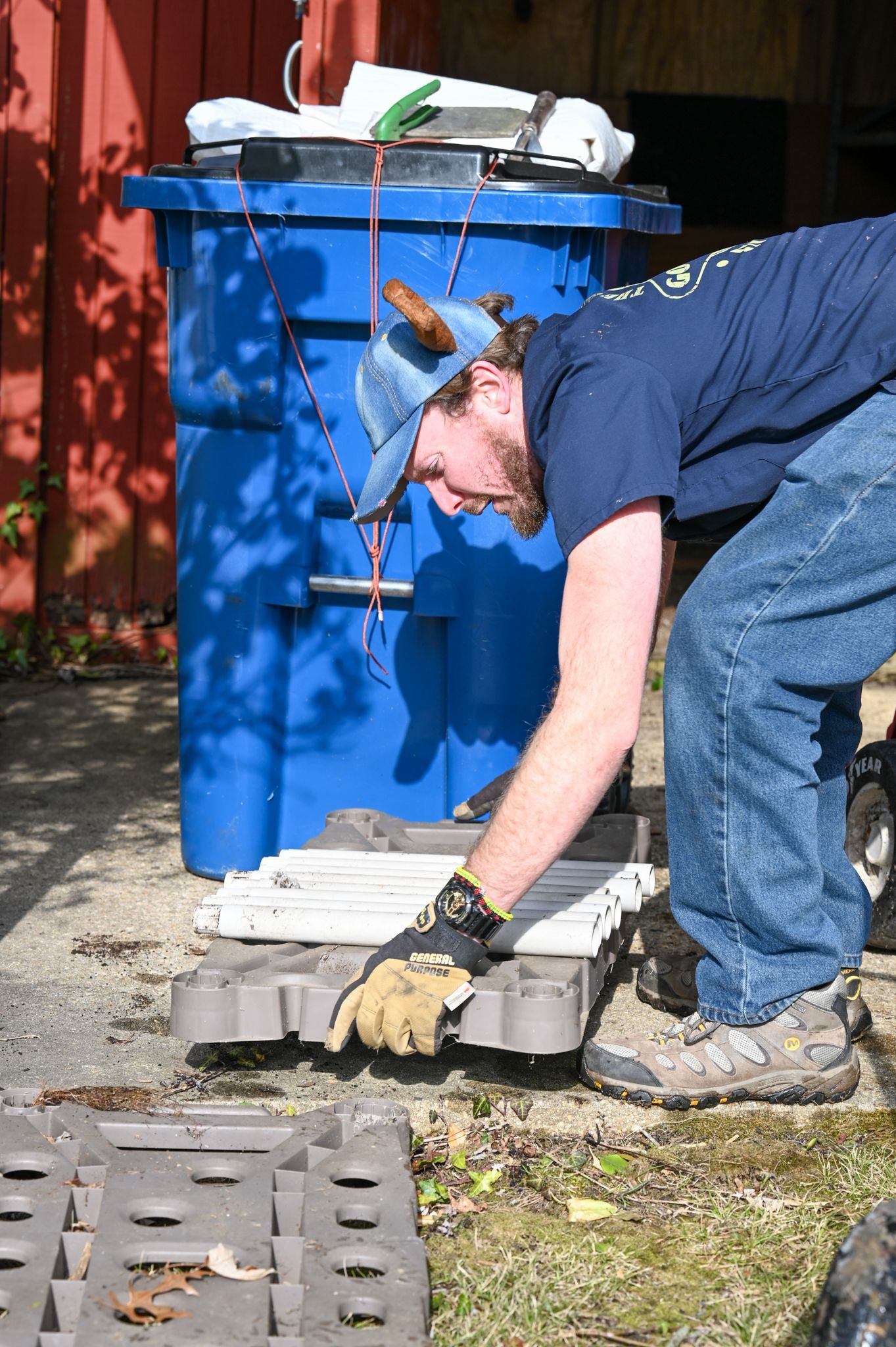 A man is kneeling down in front of a blue trash can.