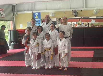 Group of martial arts students in white uniforms posing on red mats in a dojo
