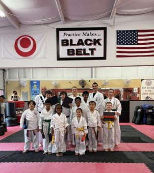 Martial arts class posing in dojo with black belt banner, American and Japanese flags, and red and black mats