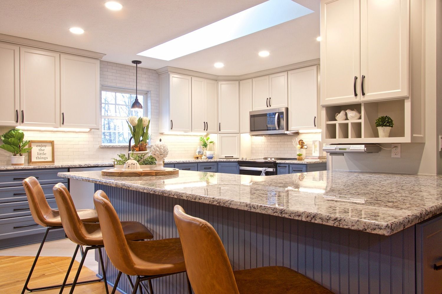 Bright modern kitchen with granite island, bar stools, white cabinets, and recessed lighting