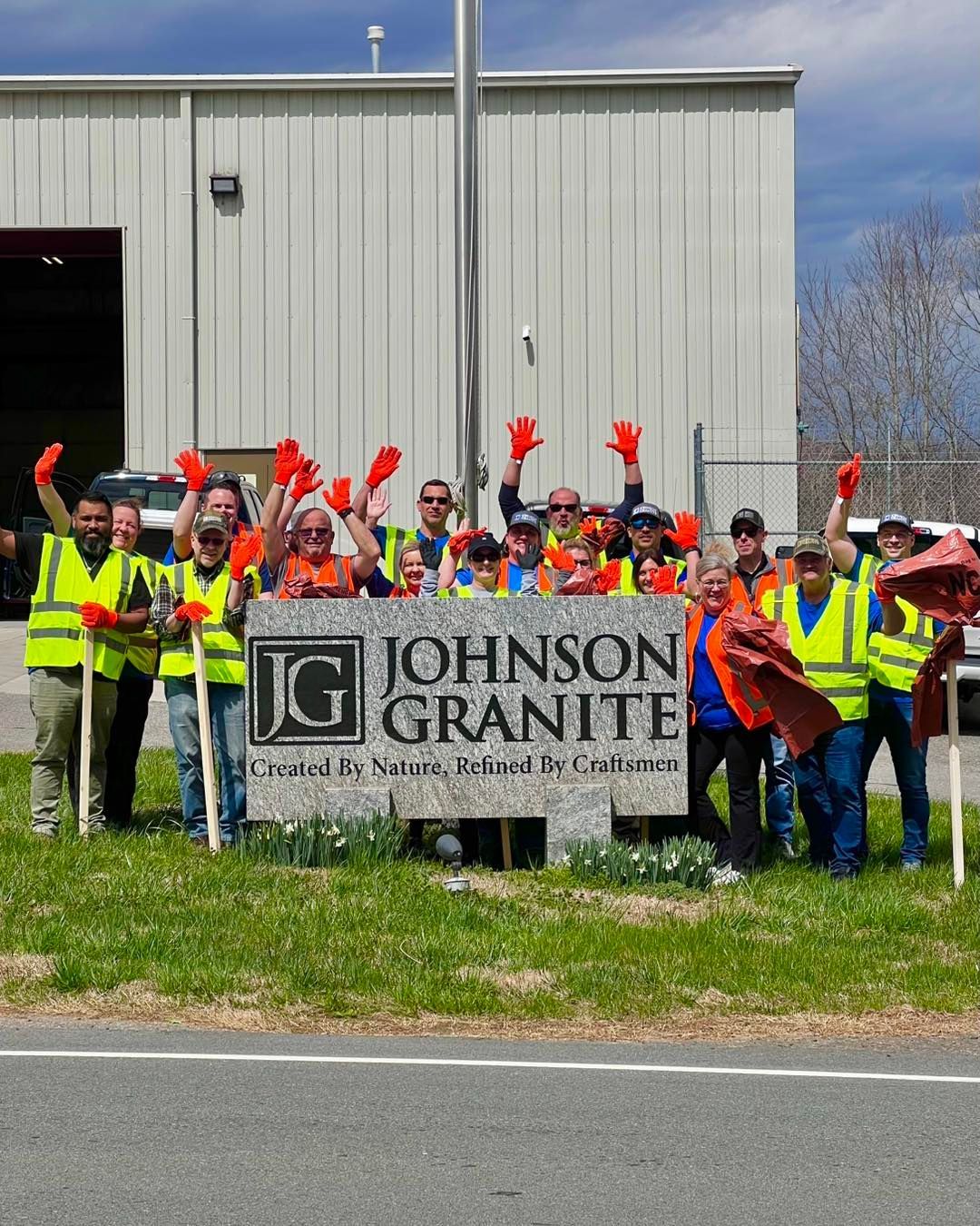 Workers in hi-vis vests serving the community waving behind a Johnson Granite sign outside a warehouse