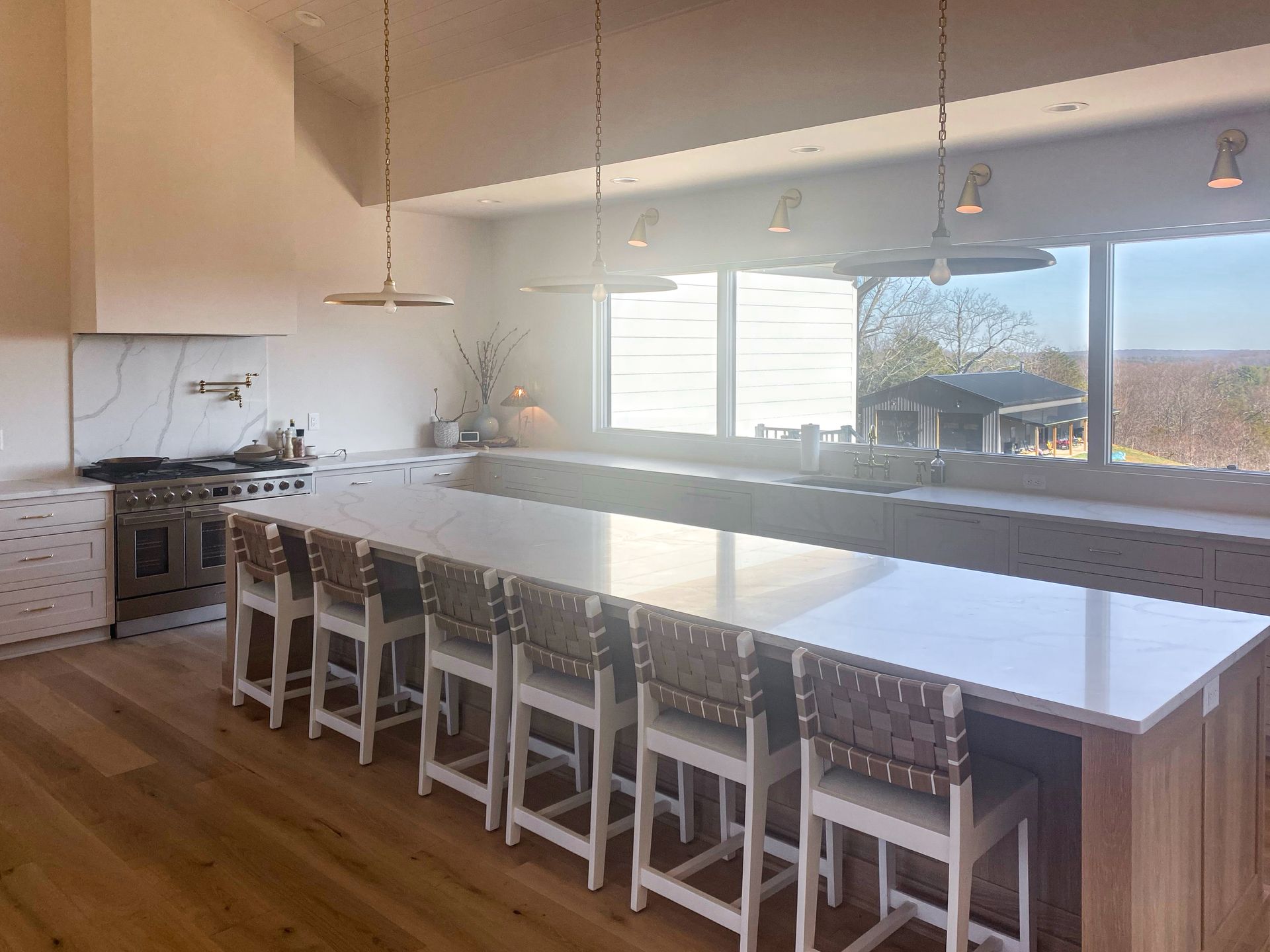 Bright modern kitchen with a large white island, bar stools, wood floors, and a window view of the mountains