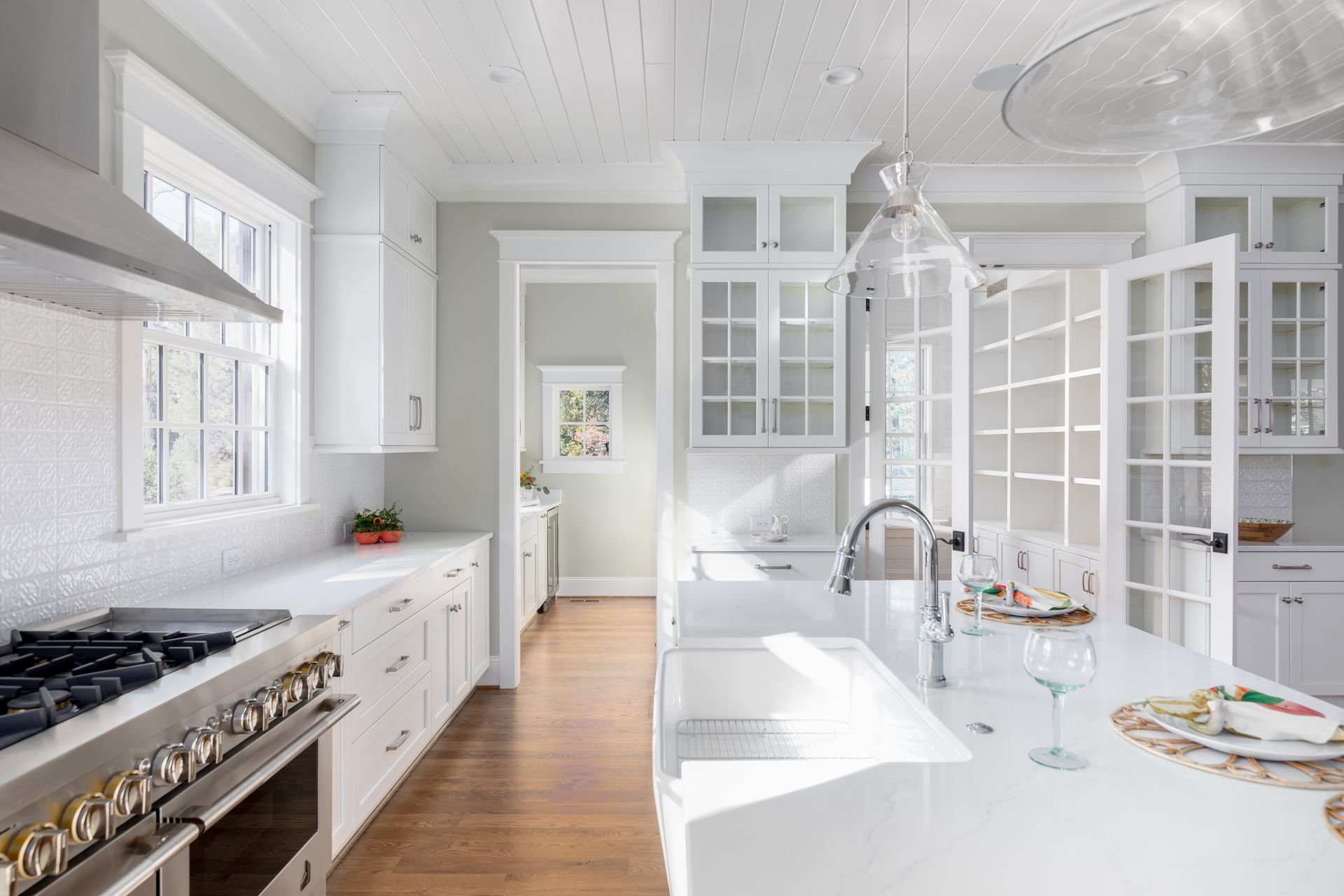 Bright white modern kitchen with island, stainless stove, glass cabinets, and wood floor