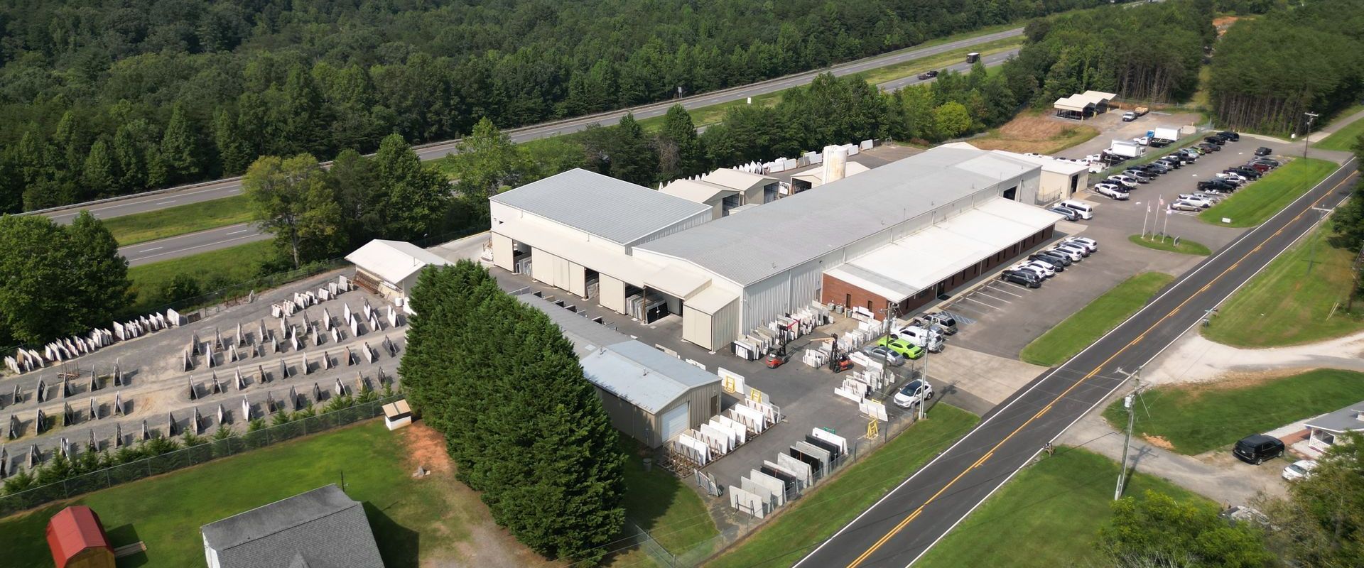 Aerial view of an Johnson Granite warehouse complex beside a road and parking lot, with trees and nearby buildings.