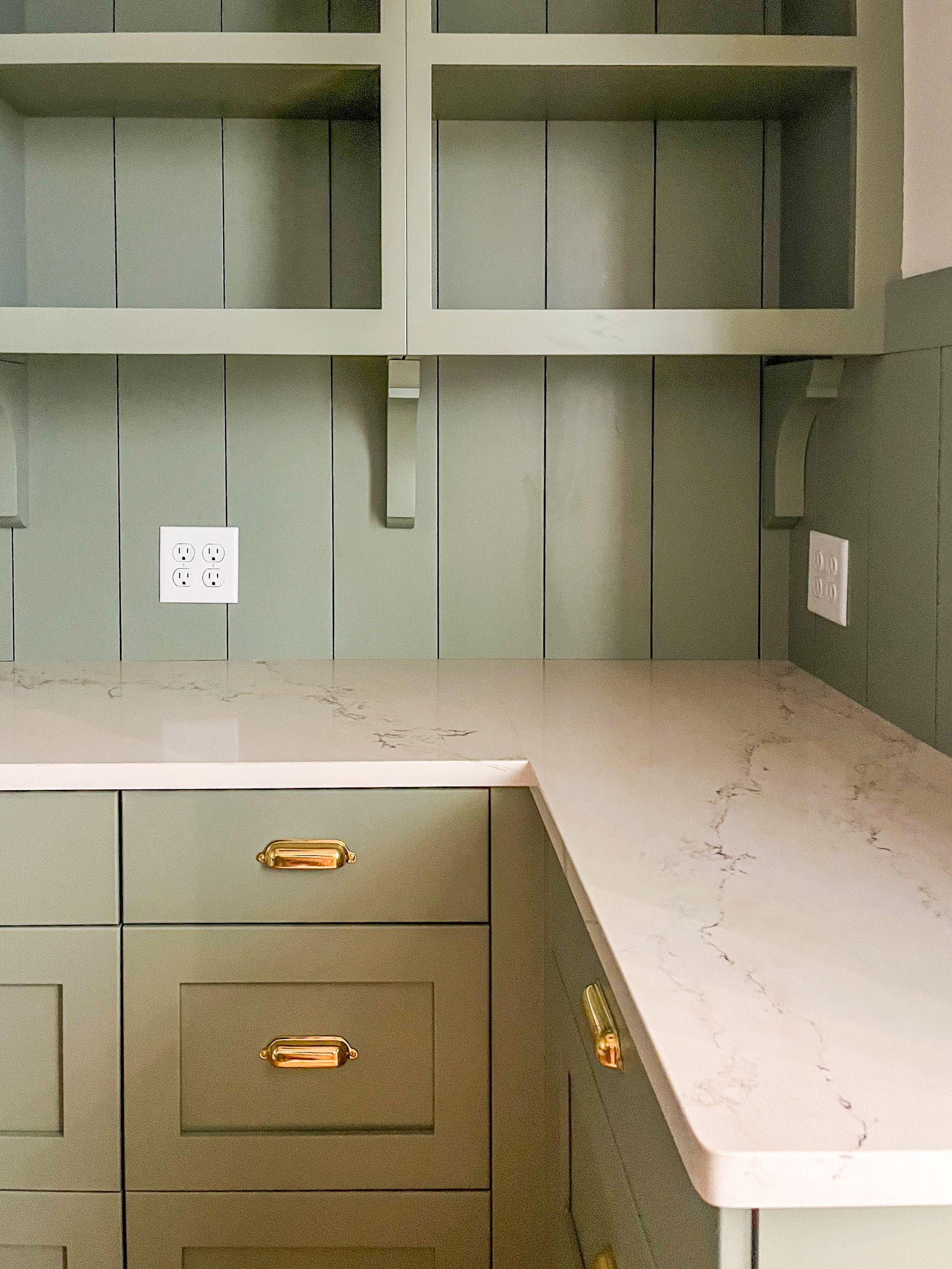 Built-in desk nook with sage green cabinets and white countertop against paneled walls.