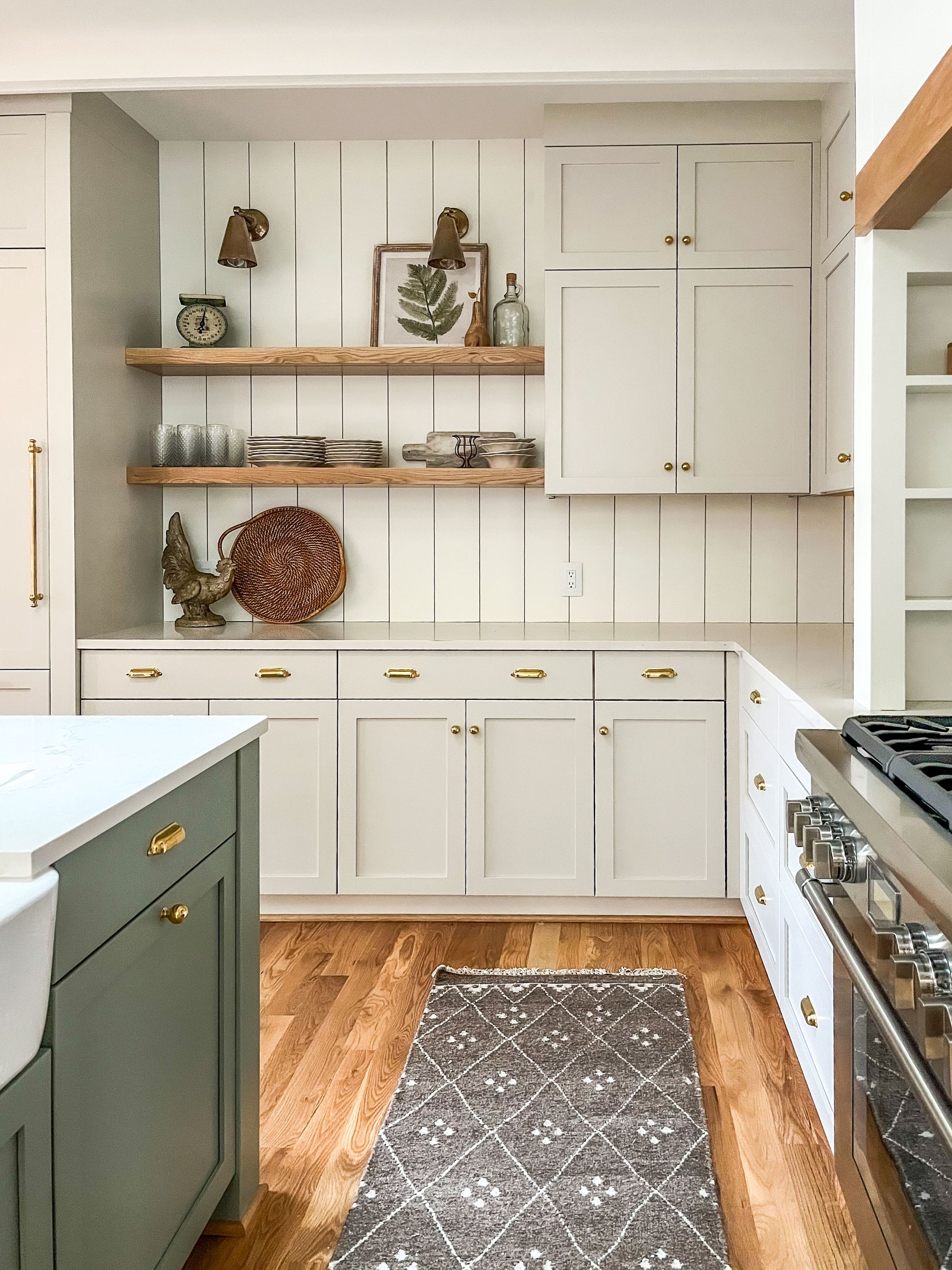 Bright kitchen with white cabinets, wood shelves, green island, and patterned rug
