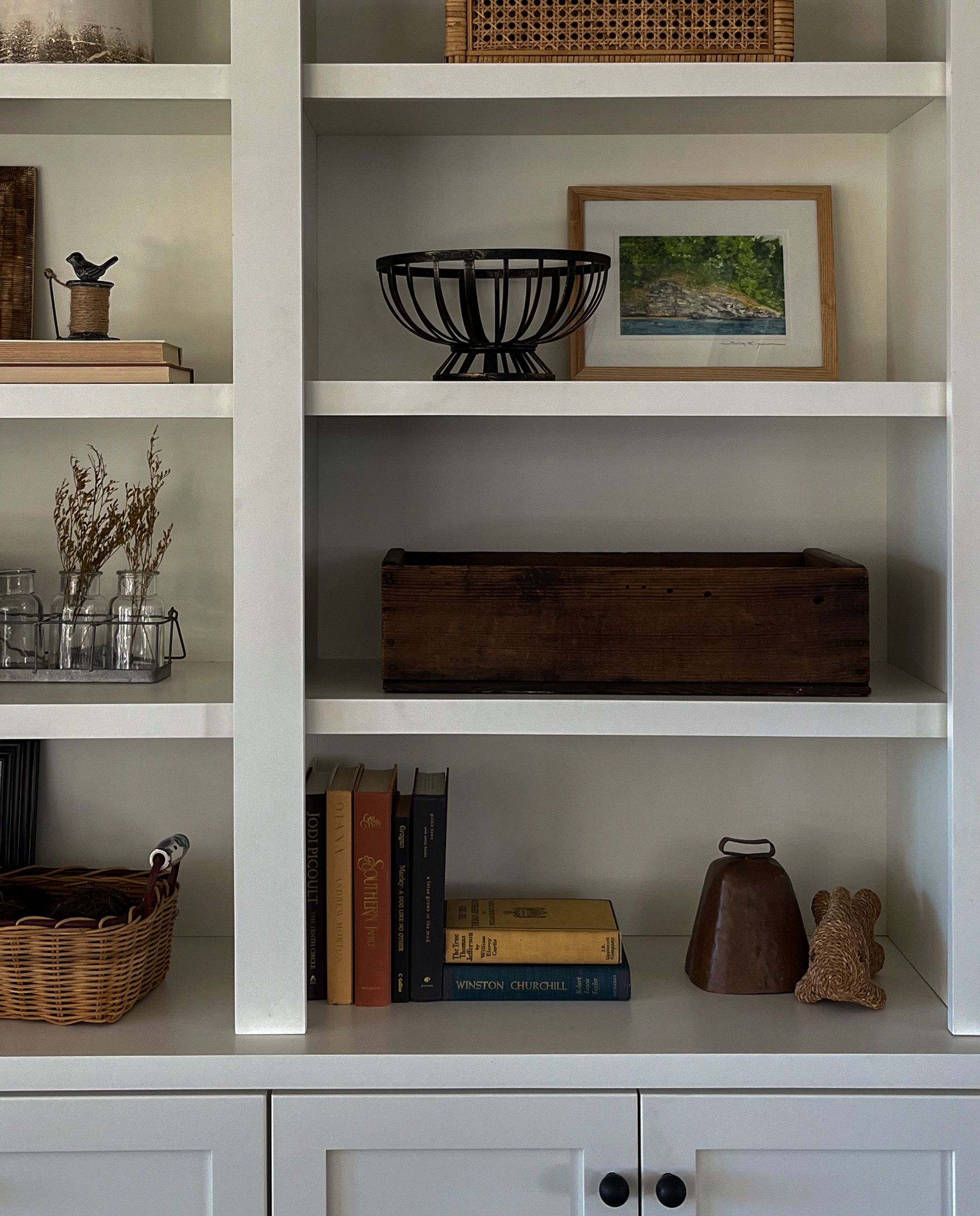 White shelving with baskets, books, framed art, and decorative objects in a home interior.