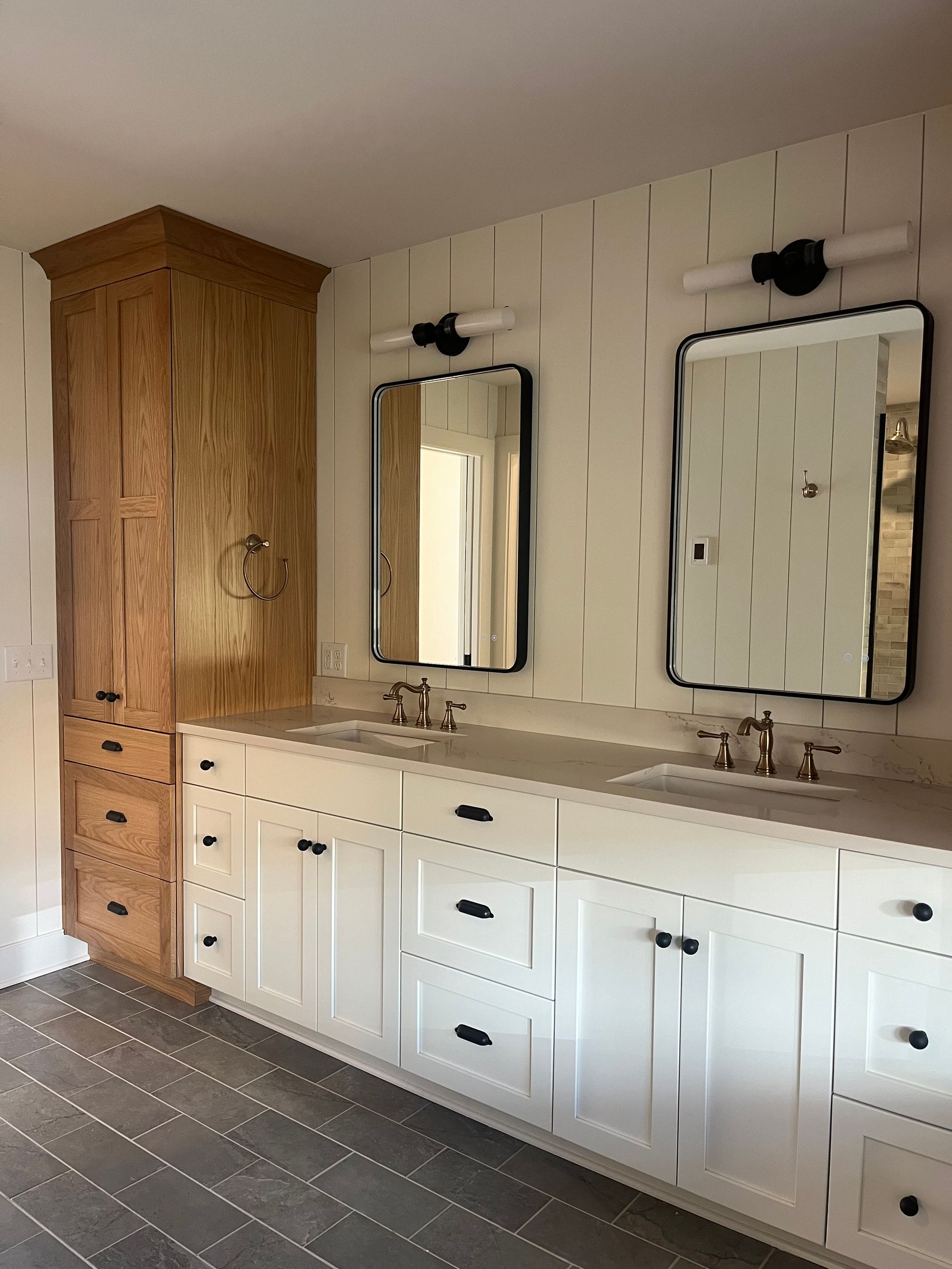 Bathroom vanity with twin mirrors, white cabinets, wood countertop, and tall wooden storage cabinet