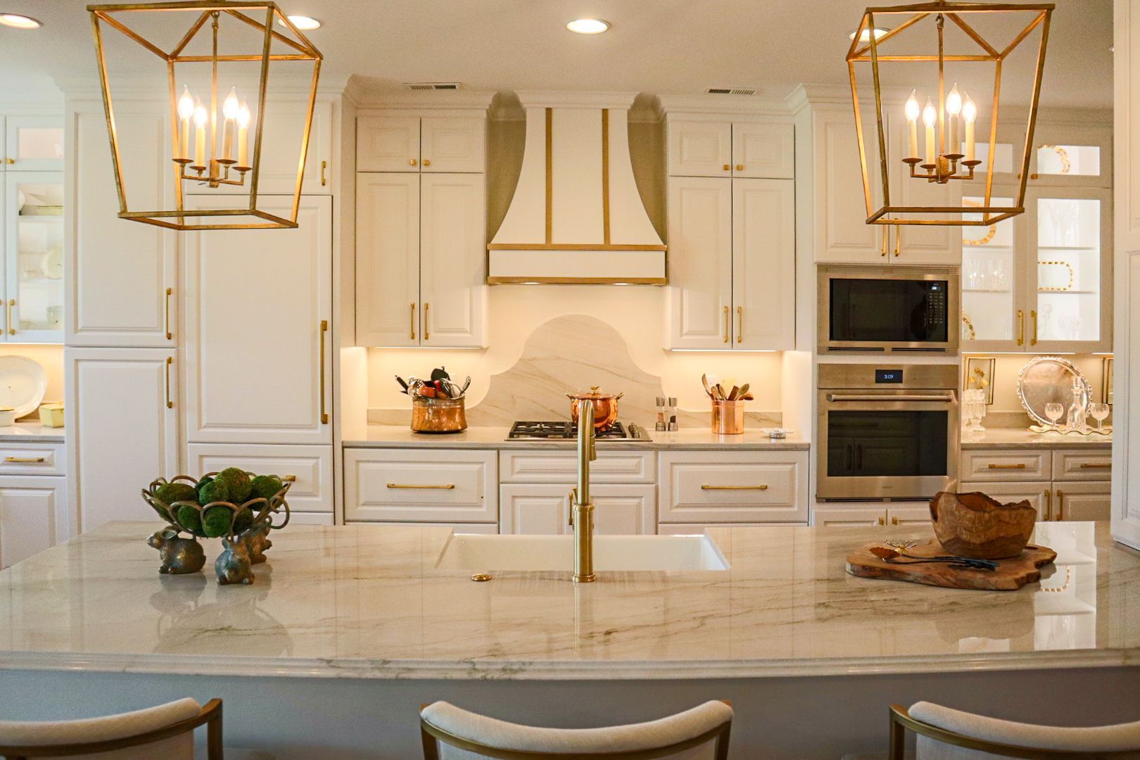 Bright white kitchen with gold pendant lights, marble island, and built-in ovens