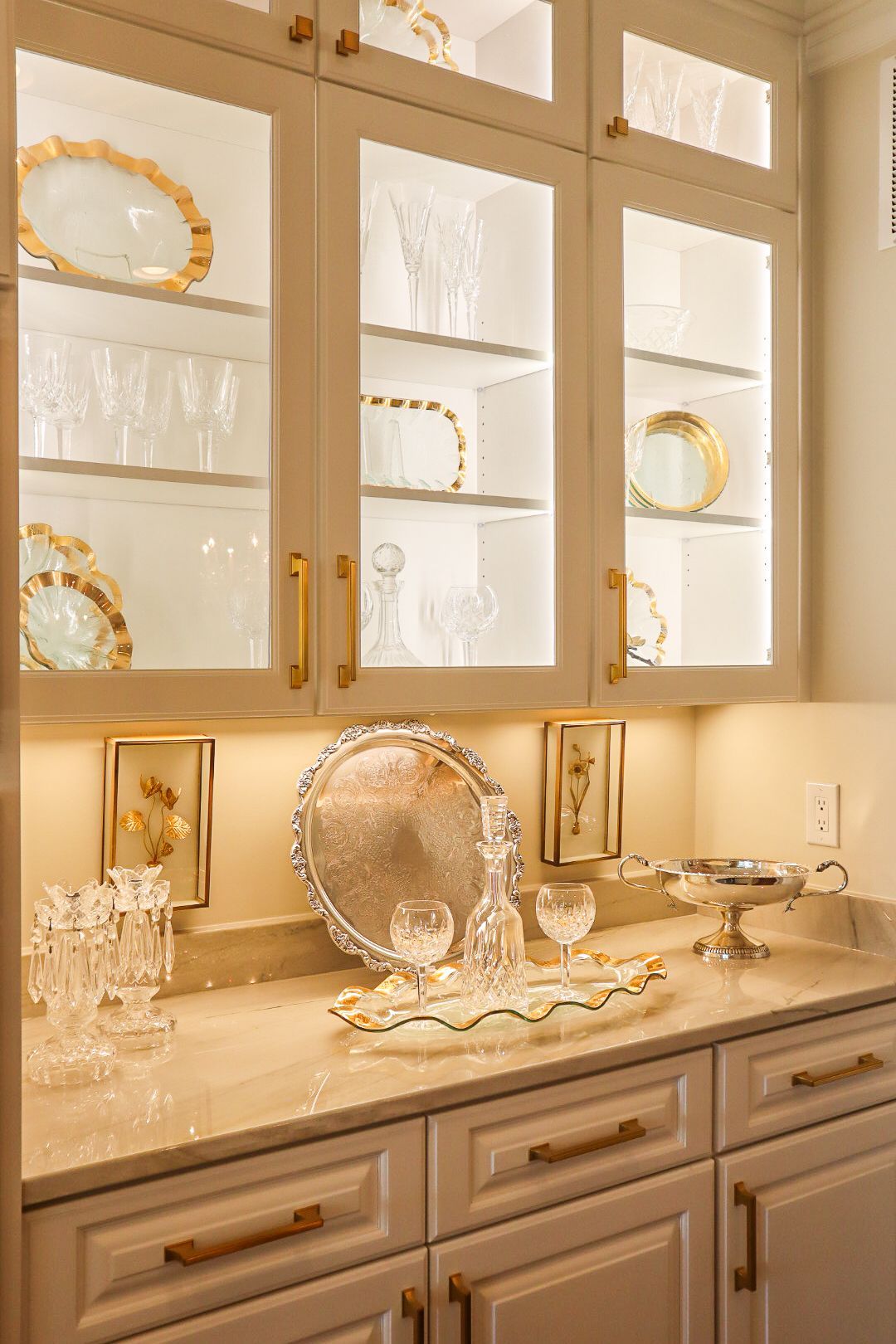 Elegant kitchen hutch with glass doors, dishes, and decorative plates above a marble countertop