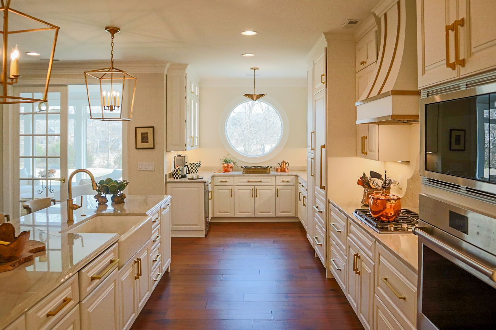 Bright white kitchen with island, hardwood floors, and a round window at the far end