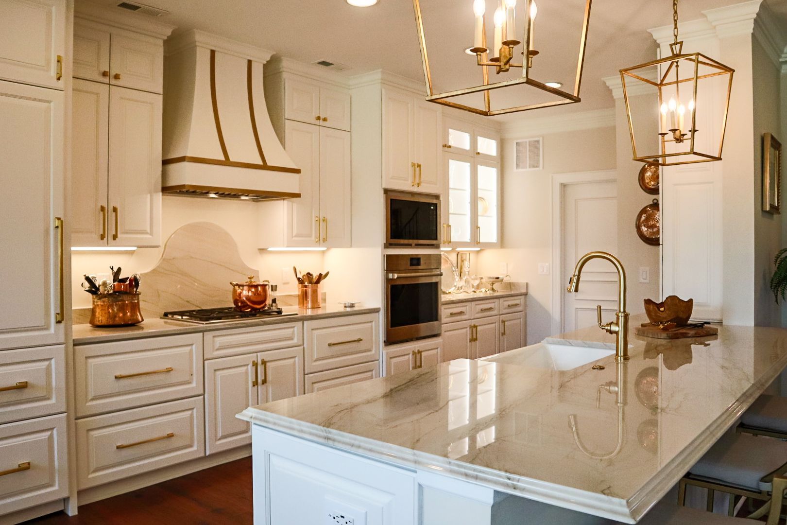 Bright white kitchen with marble island, brass pendant lights, and built-in ovens