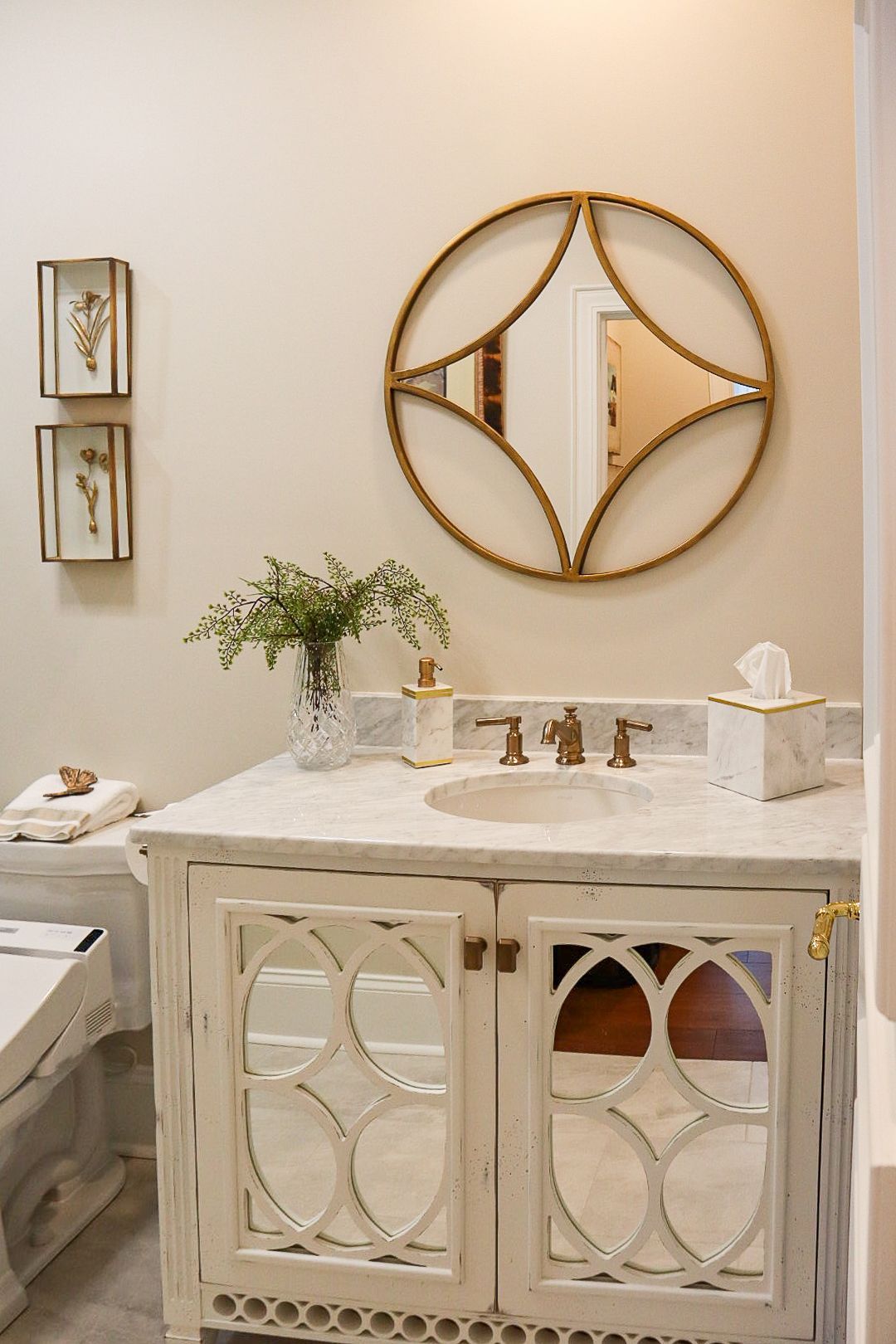 Elegant bathroom vanity with round gold mirror, white sink cabinet, and marble countertop against beige walls