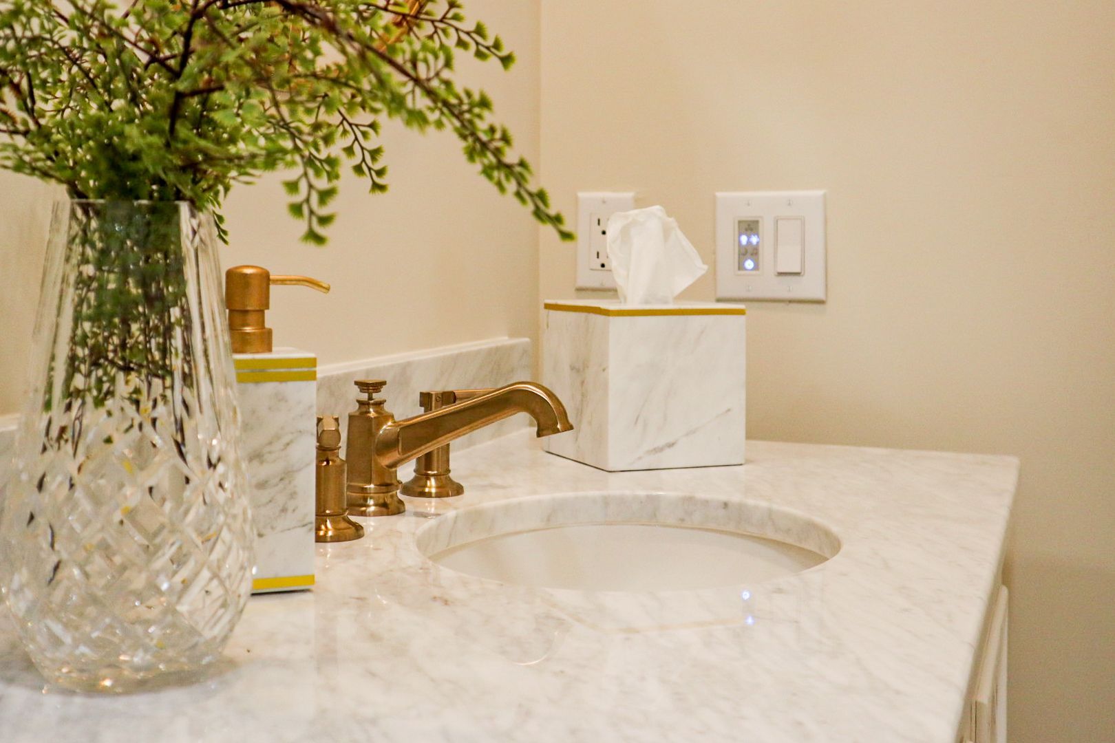 Elegant bathroom vanity with white marble counter, gold faucet, and glass vase of branches