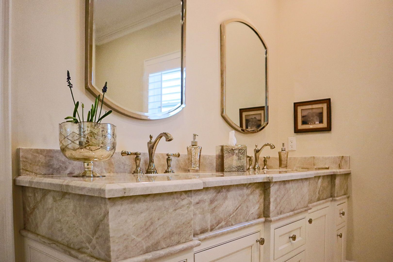 Elegant bathroom vanity with marble countertop, gold fixtures, and oval mirrors on a beige wall