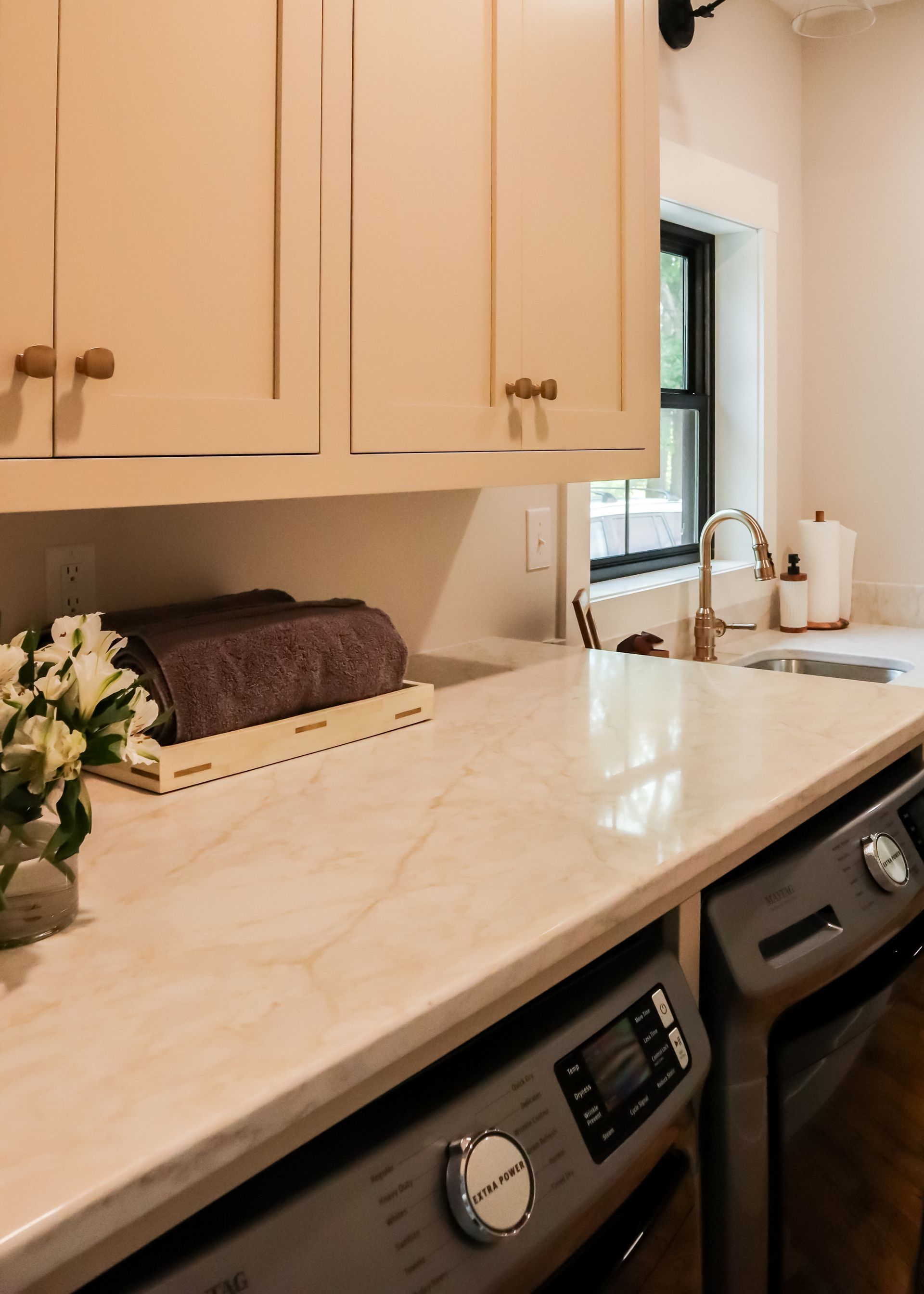 Laundry room countertop with beige cabinets, sink, and washer/dryer beneath a window