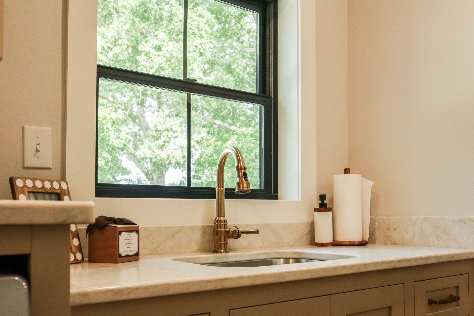 Bright kitchen sink under window with bronze faucet, soap dispenser, paper towels, and countertop items