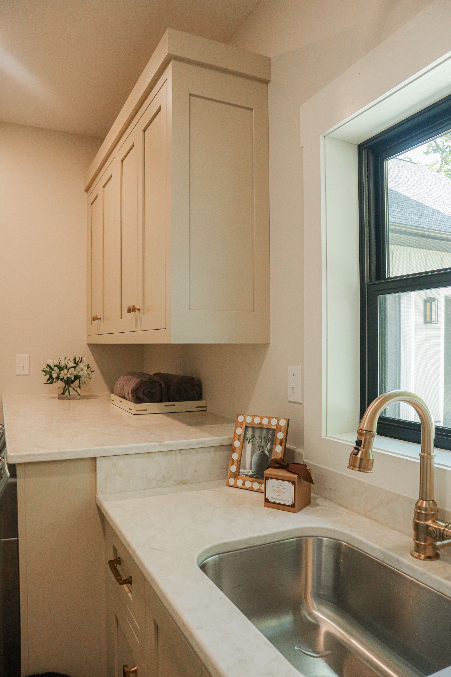 Bright kitchen with white cabinets, marble countertop, stainless sink, and window light.