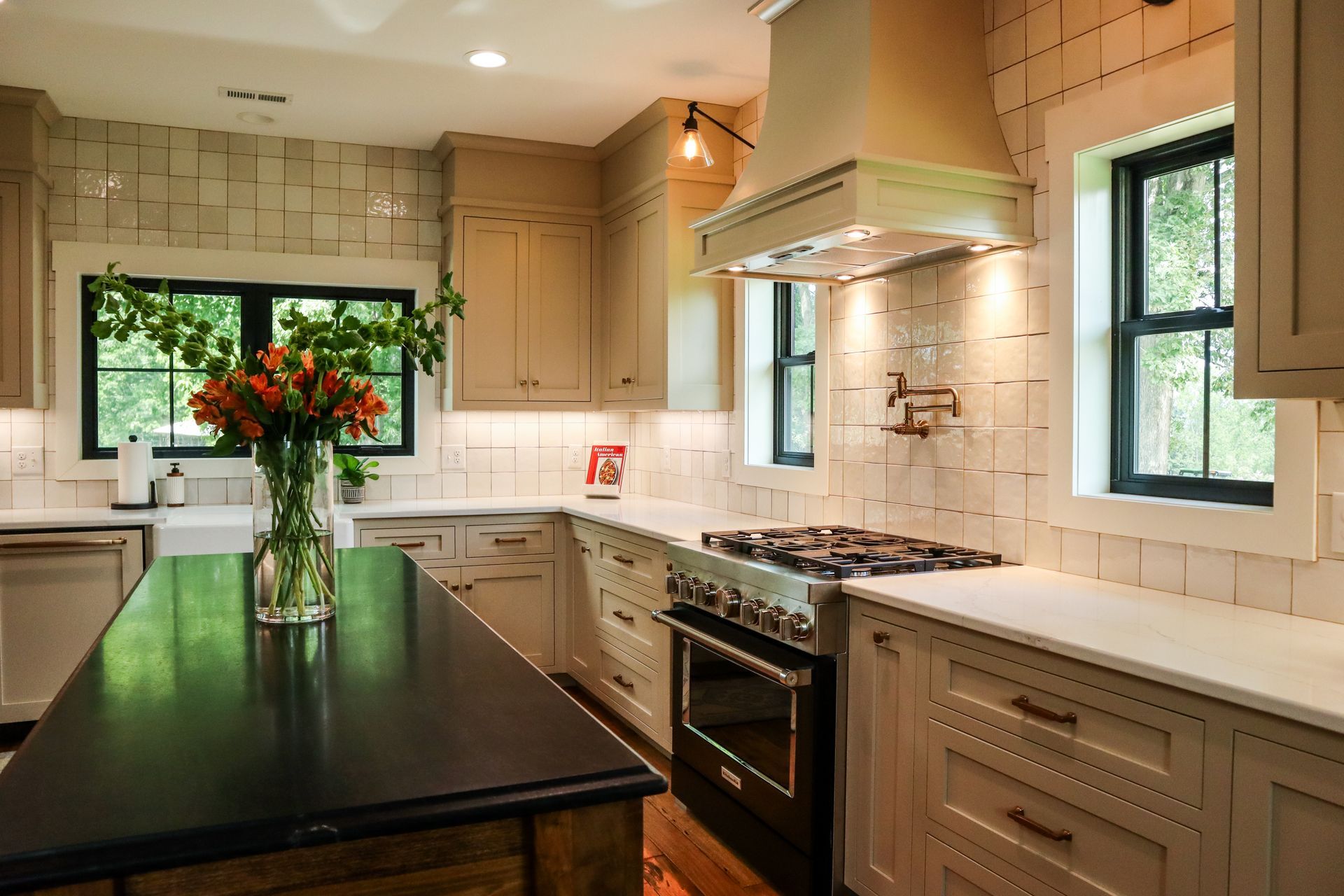 Modern kitchen with white tile, beige cabinets, black island, and a vase of orange flowers by the window