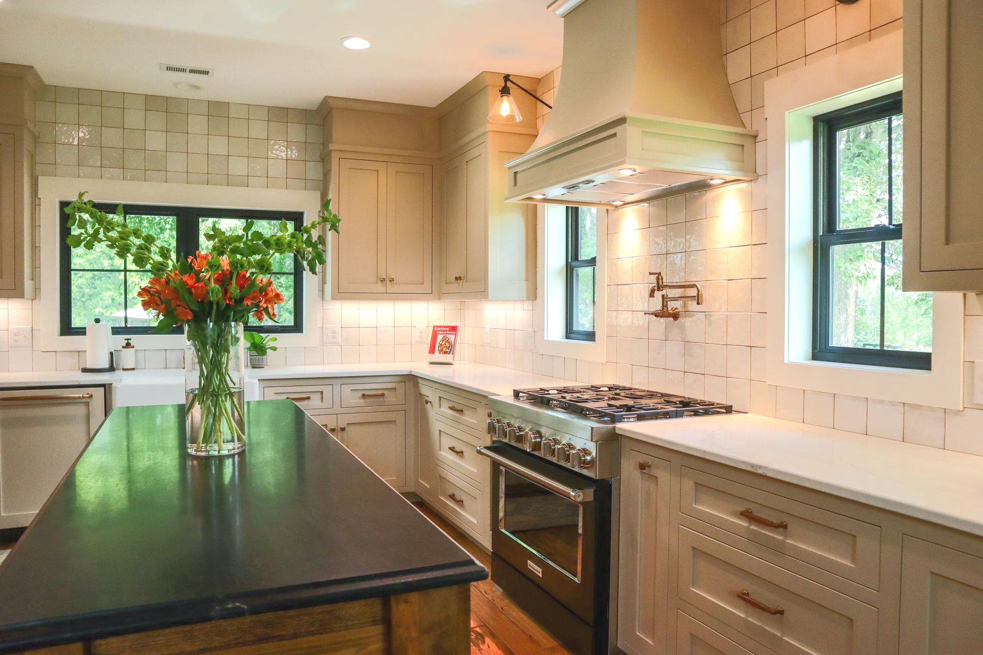 Bright modern kitchen with white cabinets, black island, stainless stove, and a vase of flowers by the window