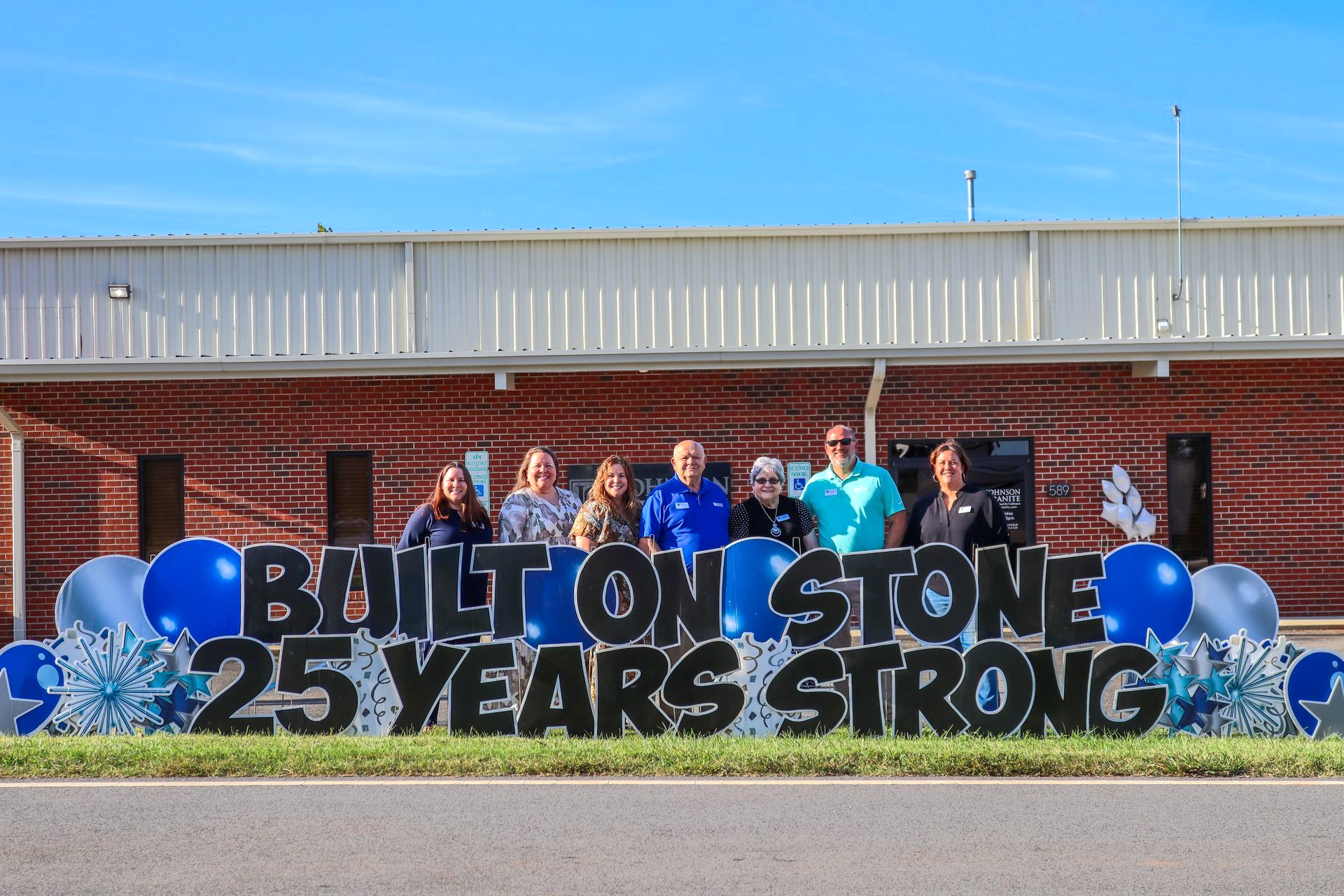 Group in front of “Built on Stone 25 Years Strong” sign with blue balloons outdoors