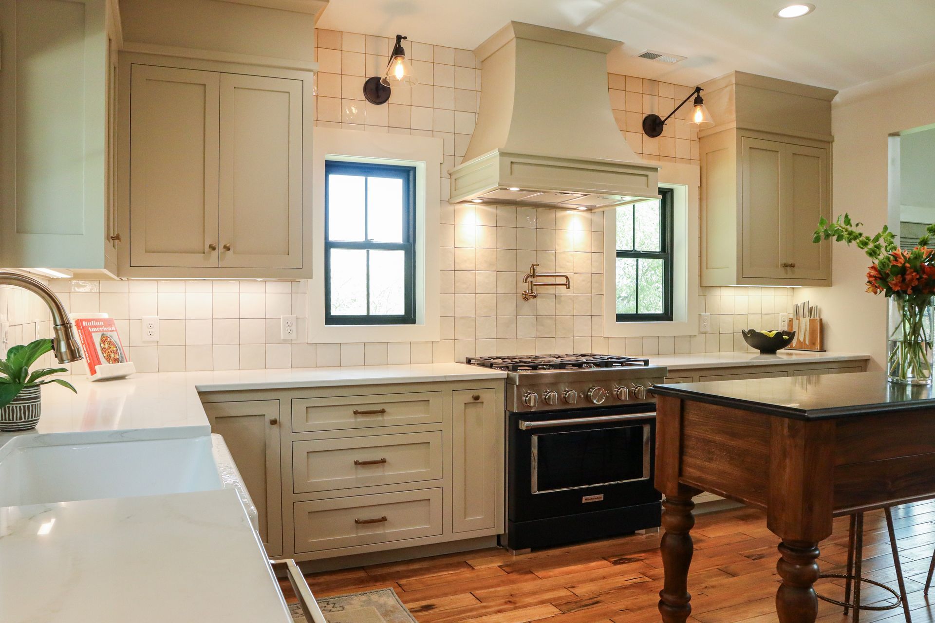 Bright farmhouse kitchen with cream cabinets, black stove, white sink, and wooden table by the window.