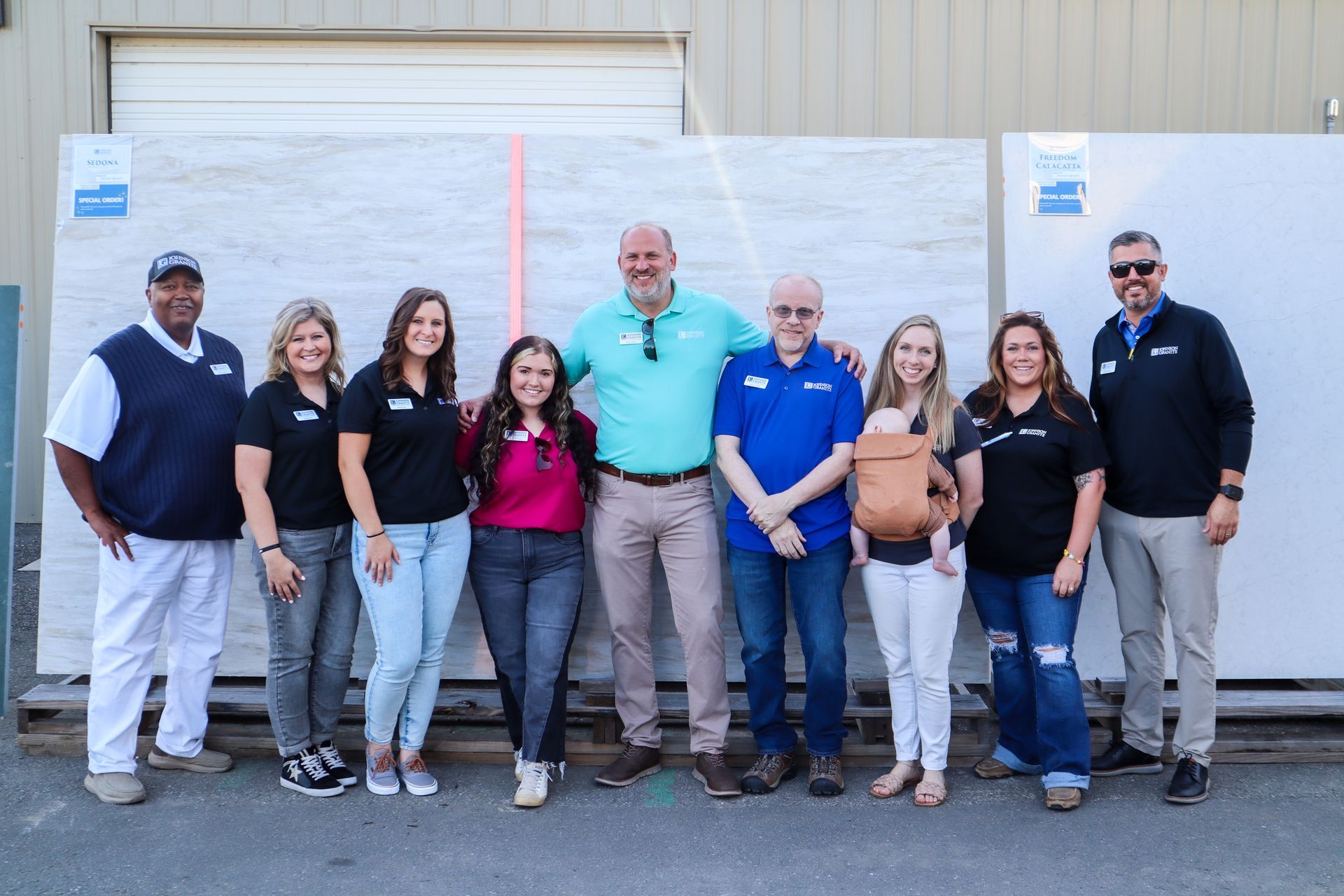 Group of JGI leaders posing outdoors in front of a white wall and garage door, smiling and standing together
