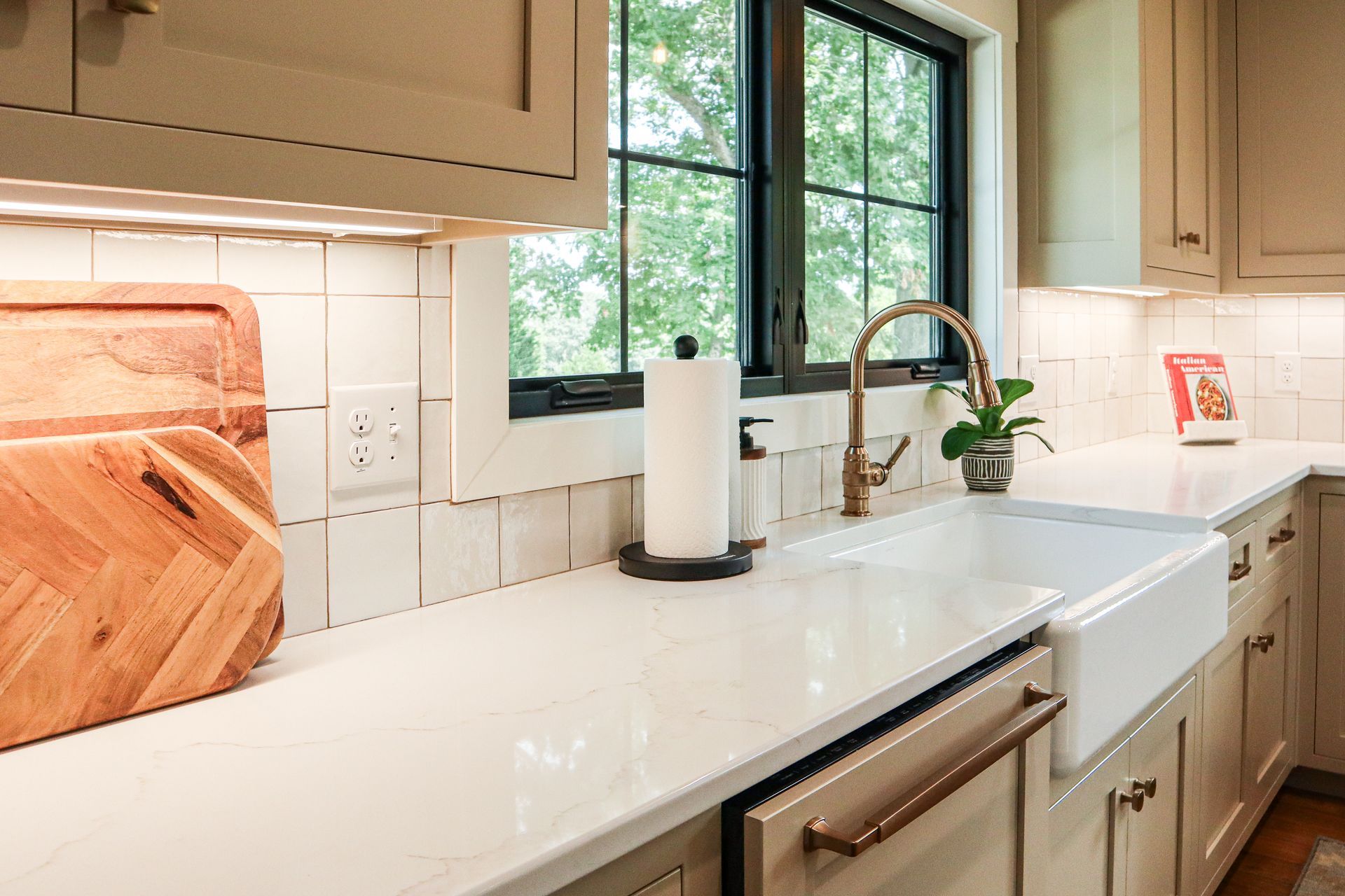 Bright kitchen countertop with sink, window, beige cabinets, and paper towel holder