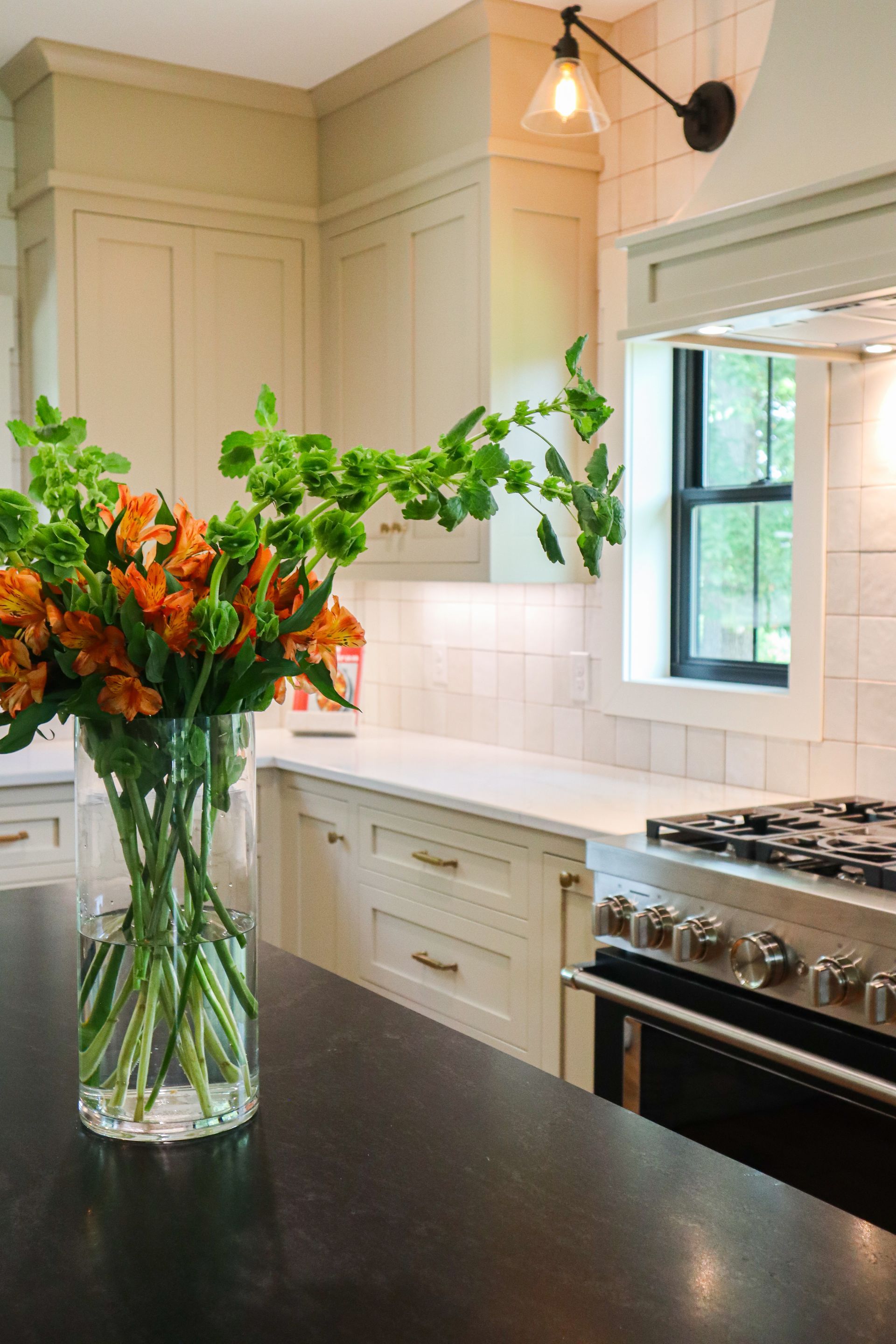 Bright kitchen with a vase of orange flowers on a dark counter beside a stainless steel stove.