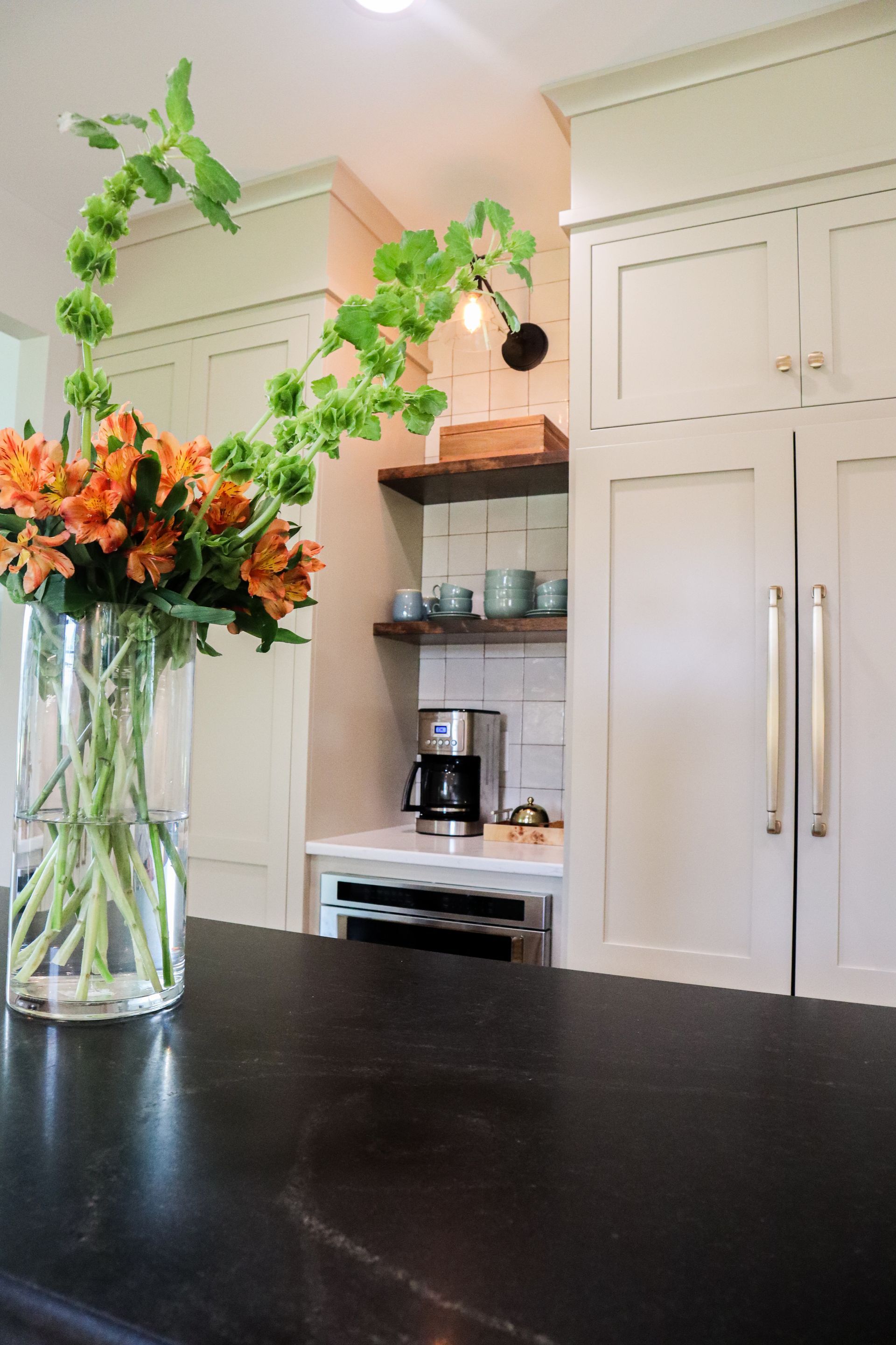 Kitchen with black countertop, cream cabinets, glass vase of orange flowers, and hanging green vine decor