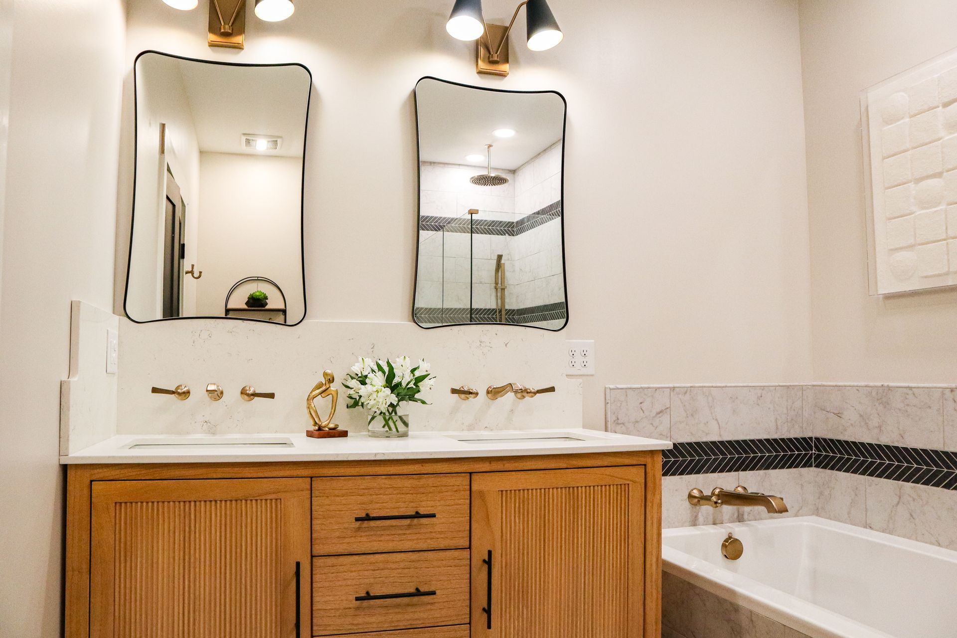 Bright bathroom with wooden vanity, two mirrors, white walls, and a bathtub on the right.