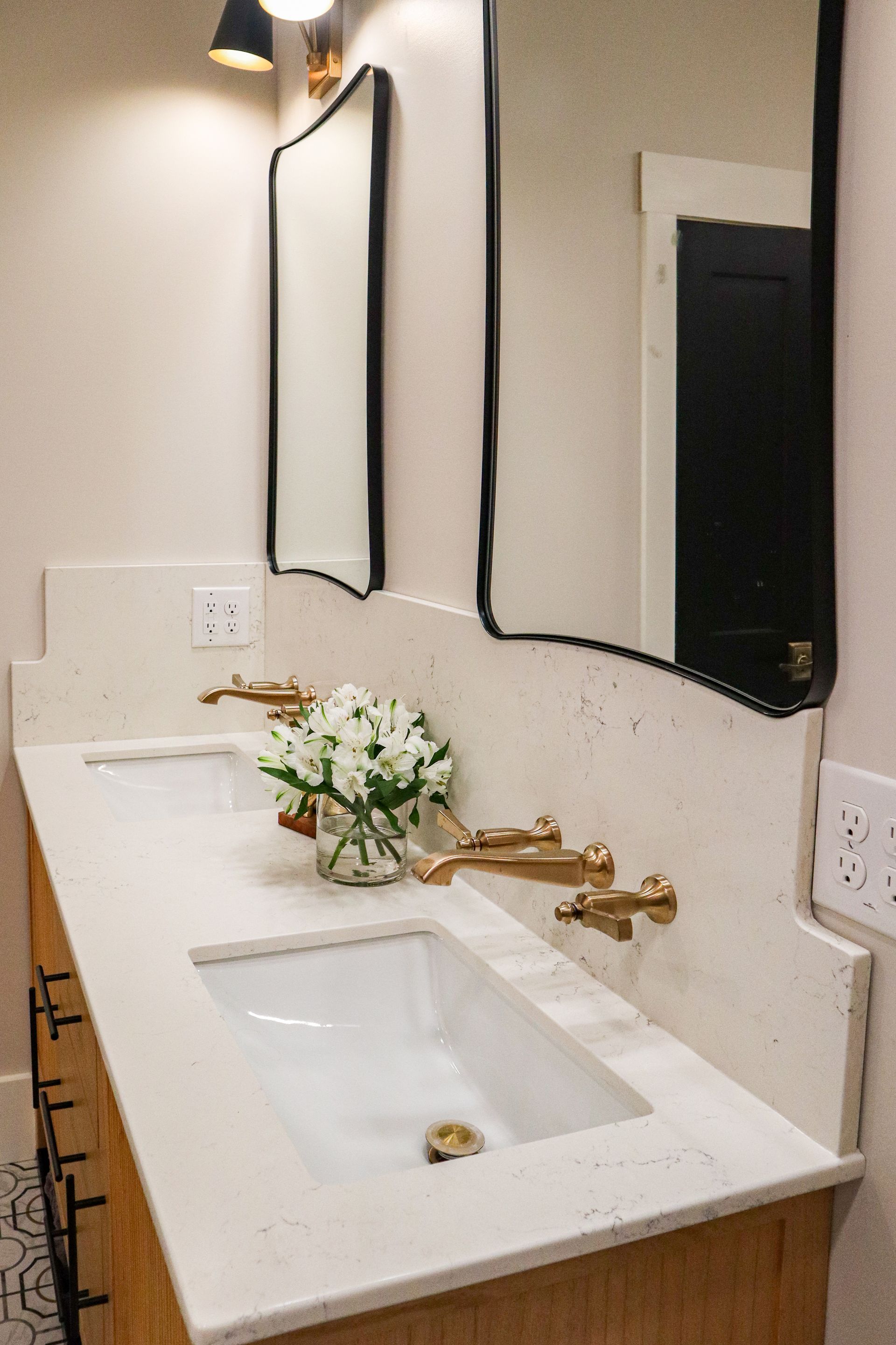 Modern bathroom vanity with white sink, gold faucets, mirror, and a small flower arrangement