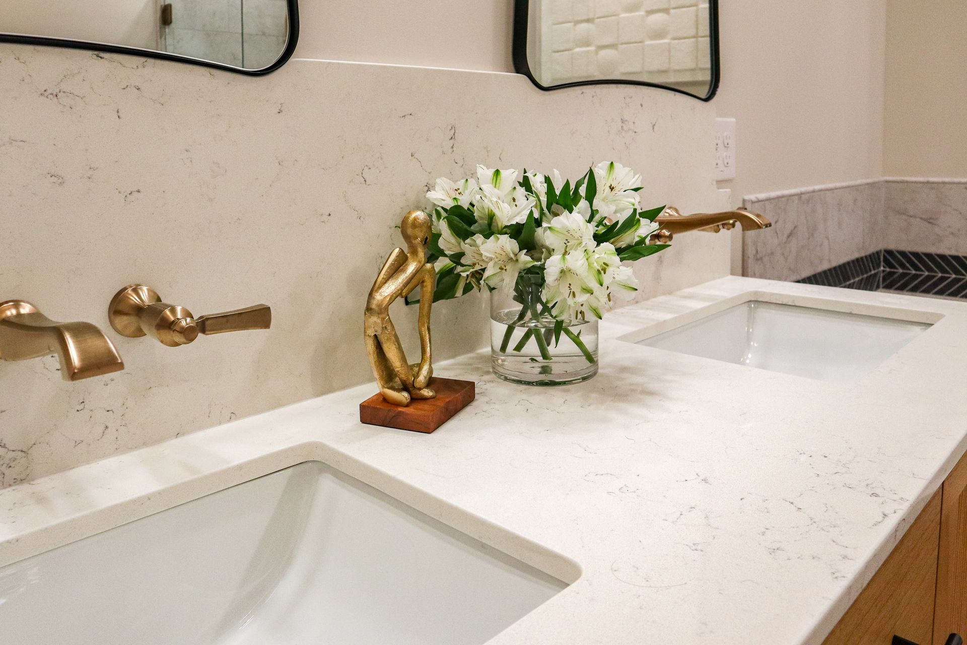 Modern bathroom vanity with double sinks, brass faucets, and a white flower arrangement on the counter