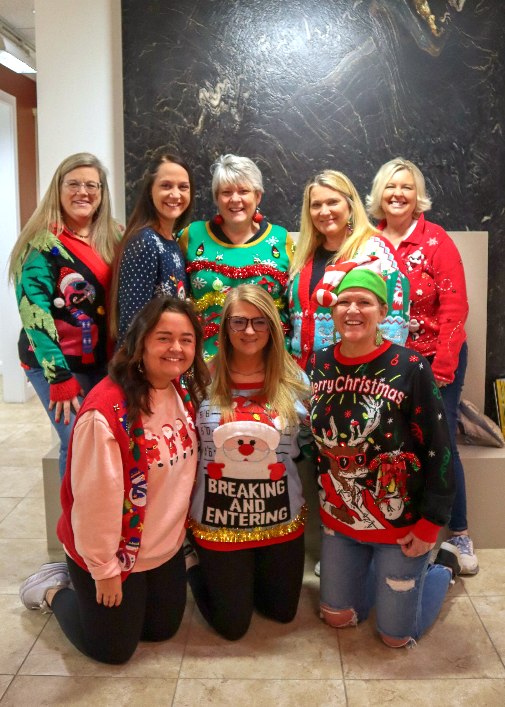 Group of people posing indoors in festive holiday sweaters, smiling for a photo.