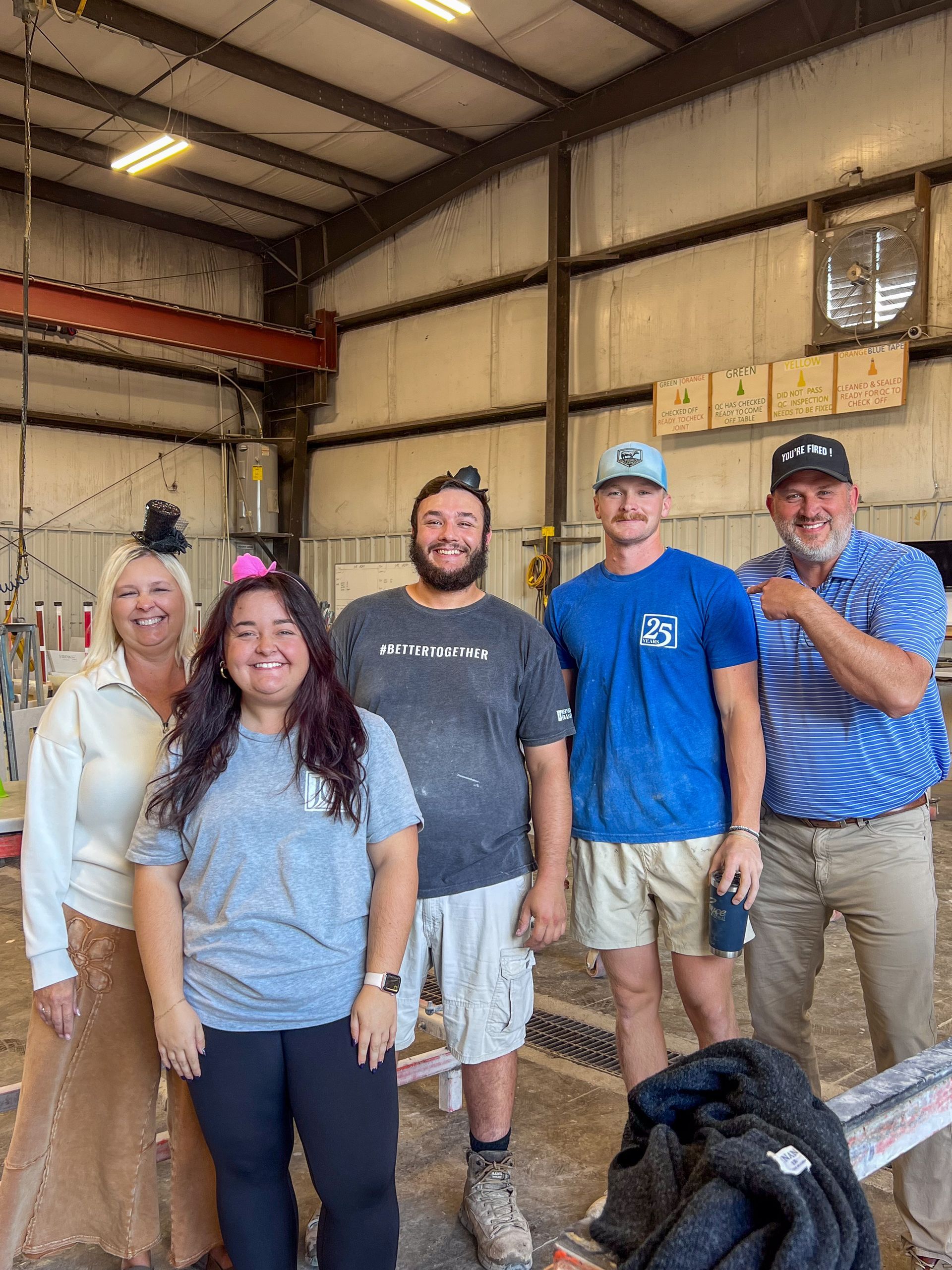 Five people standing in a warehouse, smiling near stacked boxes and a large fan.