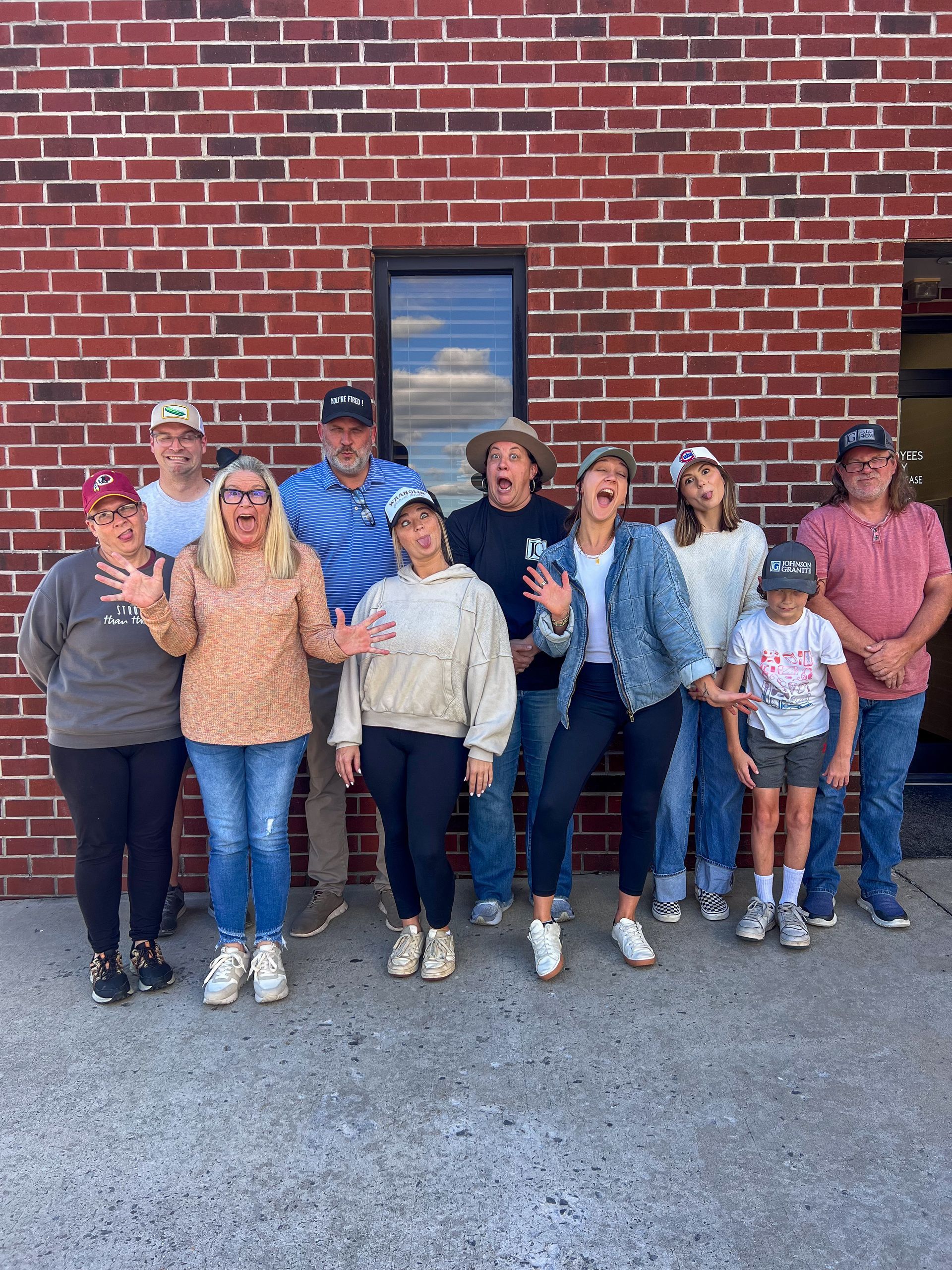 Group of people posing outside in front of a brick wall, with one person holding a small child.