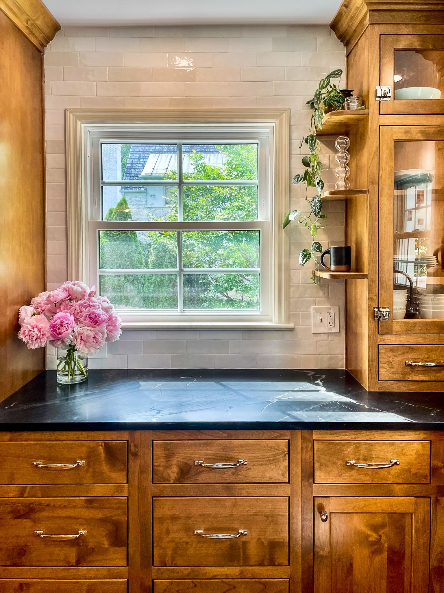 Kitchen window over black countertop with pink flowers and wooden cabinets