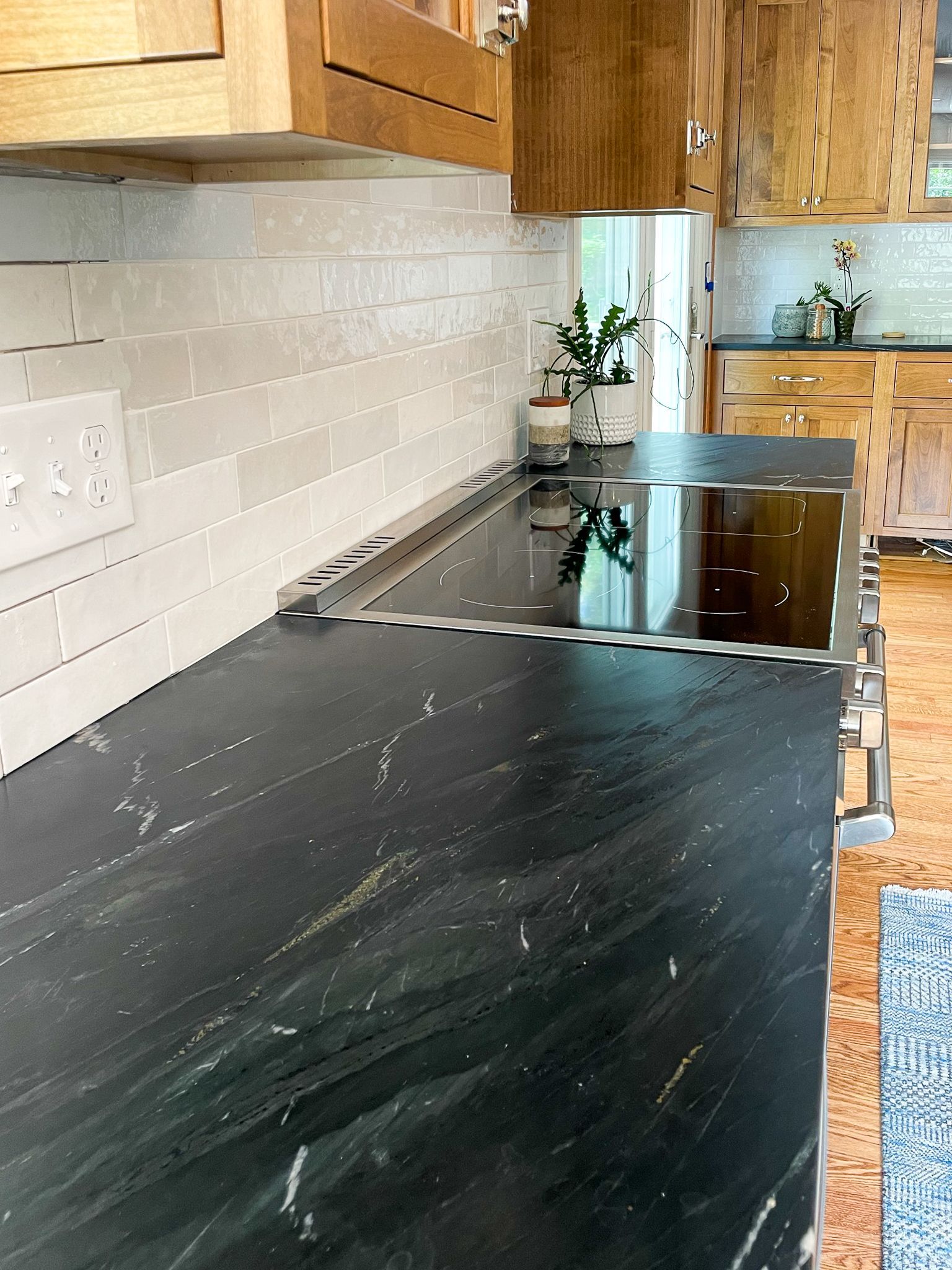 Kitchen countertop with black stone surface, stovetop, white tile backsplash, and wooden cabinets