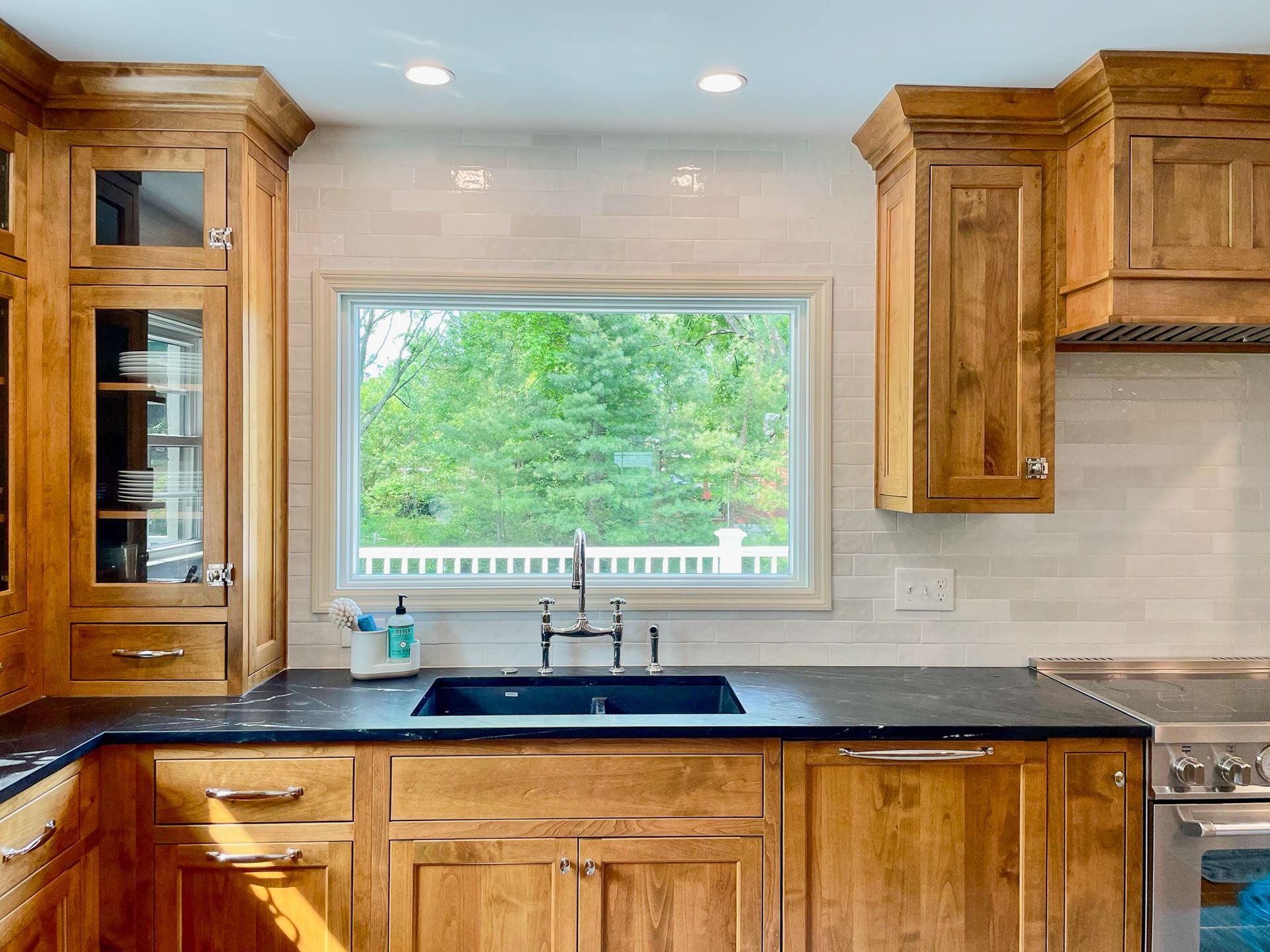 Wooden kitchen with black countertops and a large window over the sink showing green trees outside