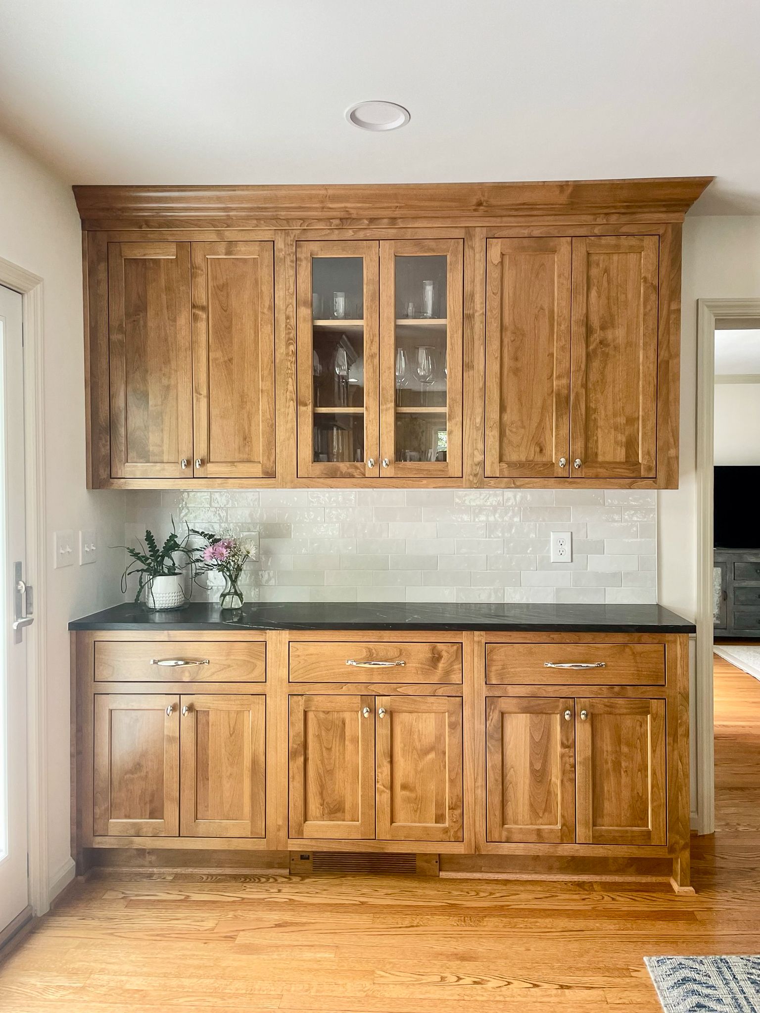 Built-in wooden kitchen cabinet with glass doors, dark countertop, and flowers on the left side.