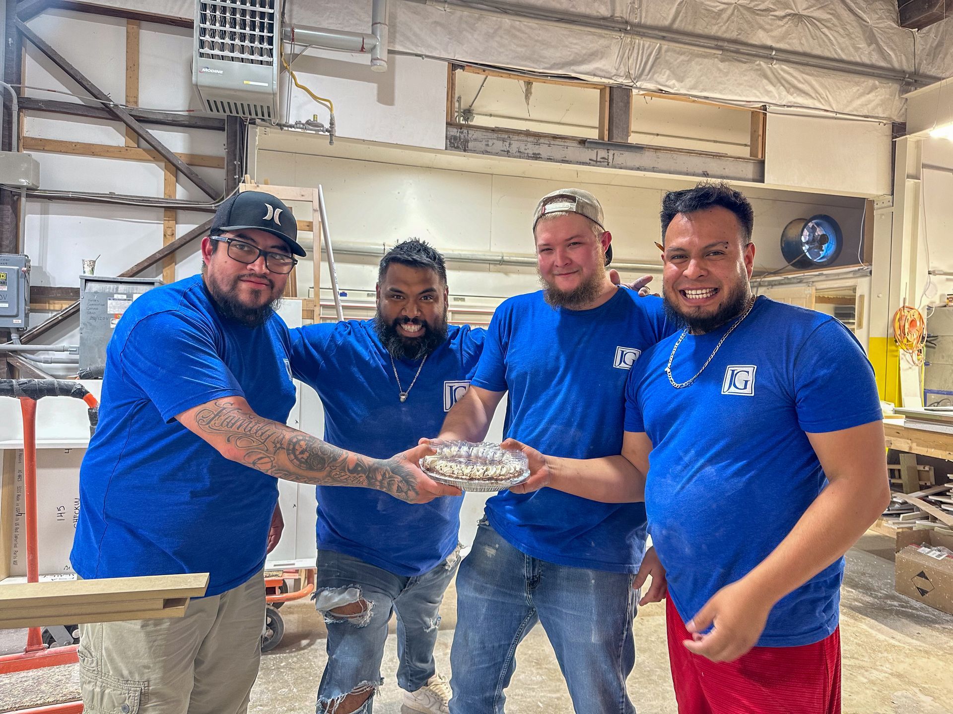 Four employees  in blue shirts stack hands in a warehouse, smiling during a team moment.