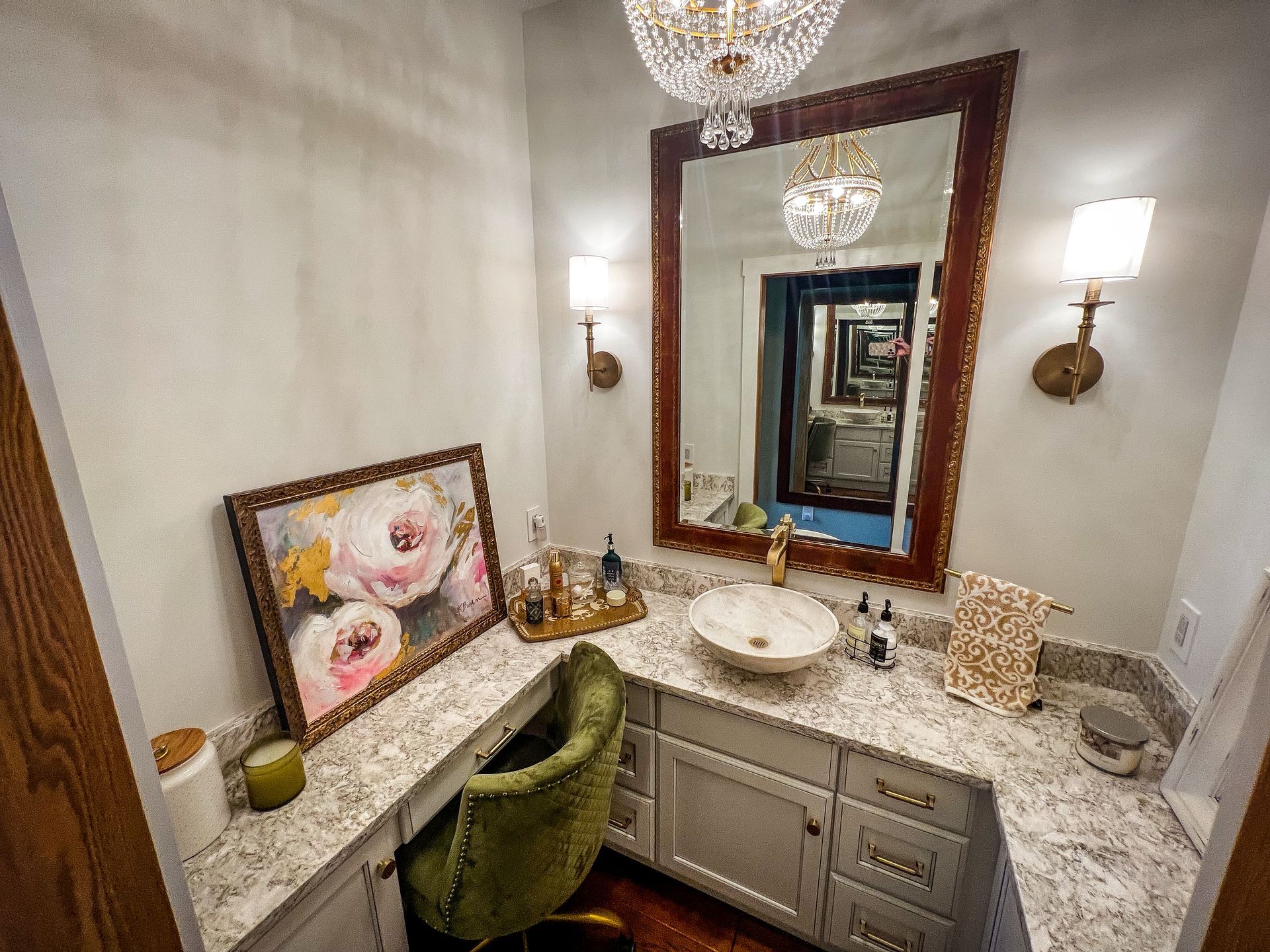 Elegant vanity nook with floral chair, marble countertop, large mirror, and wall sconces