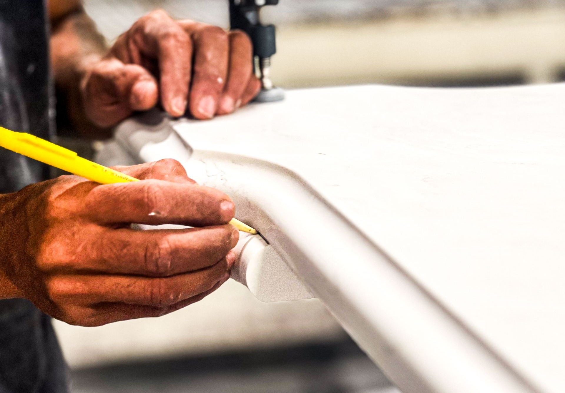 Hands using a yellow pencil to mark a white material on a work surface