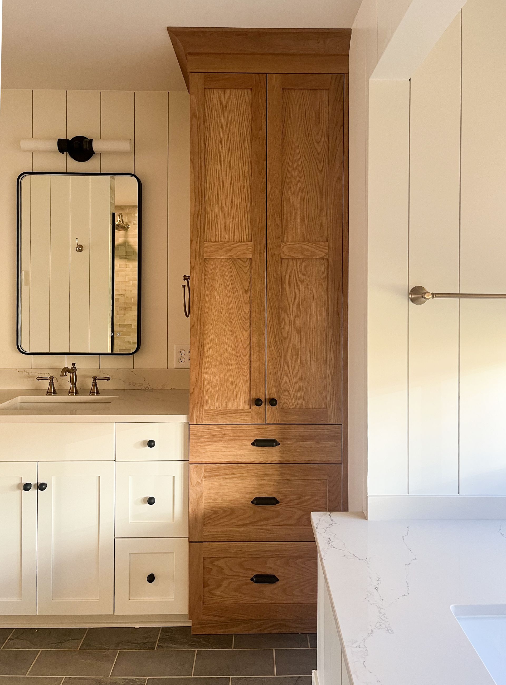 Bathroom with white vanity, mirror, and tall wood cabinet against cream walls.